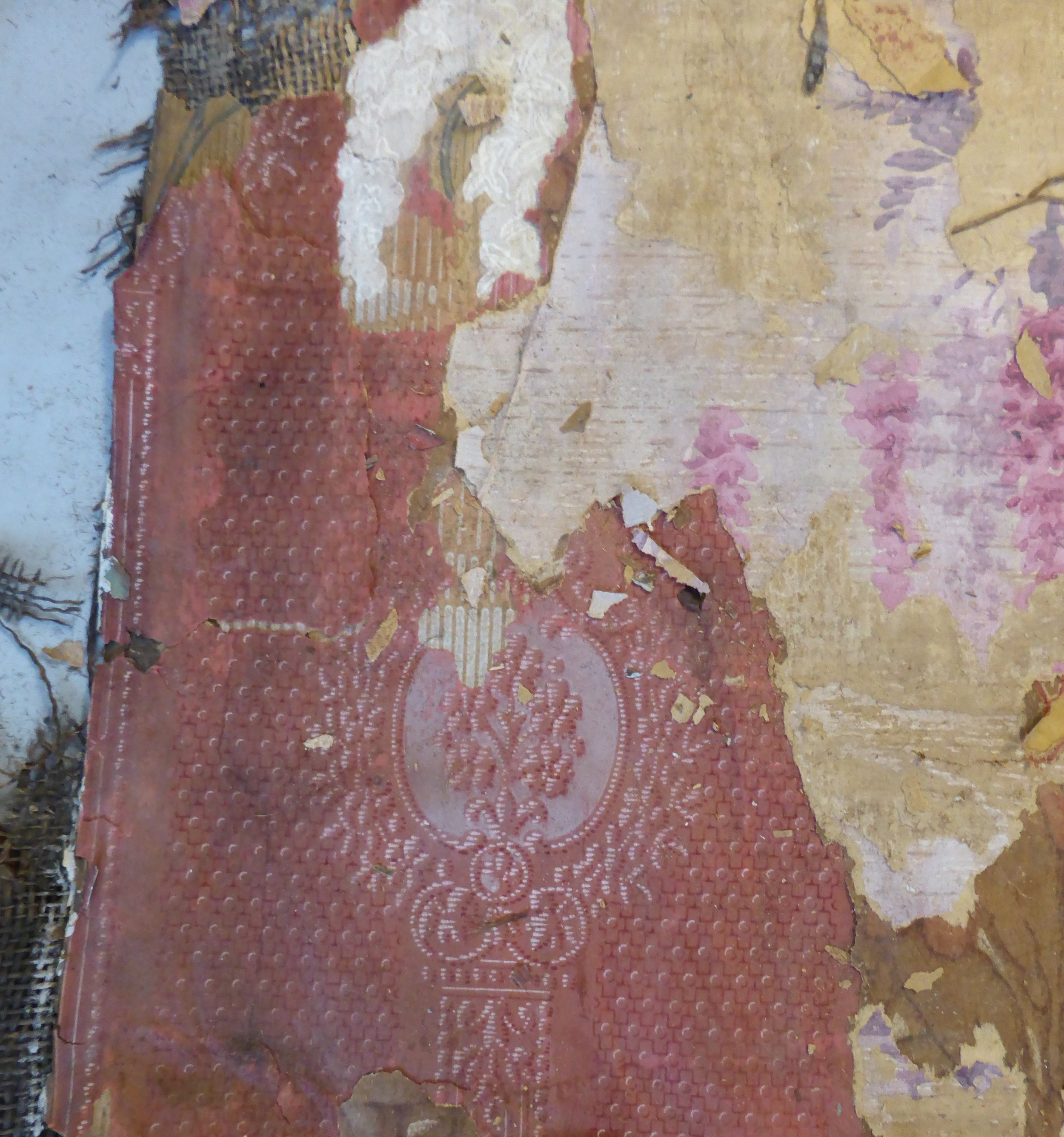 Layers of wallpaper. Largest is red, appears embossed with floral/foliage vignettes - red. Second paper appears to be red & purple delphiniums.