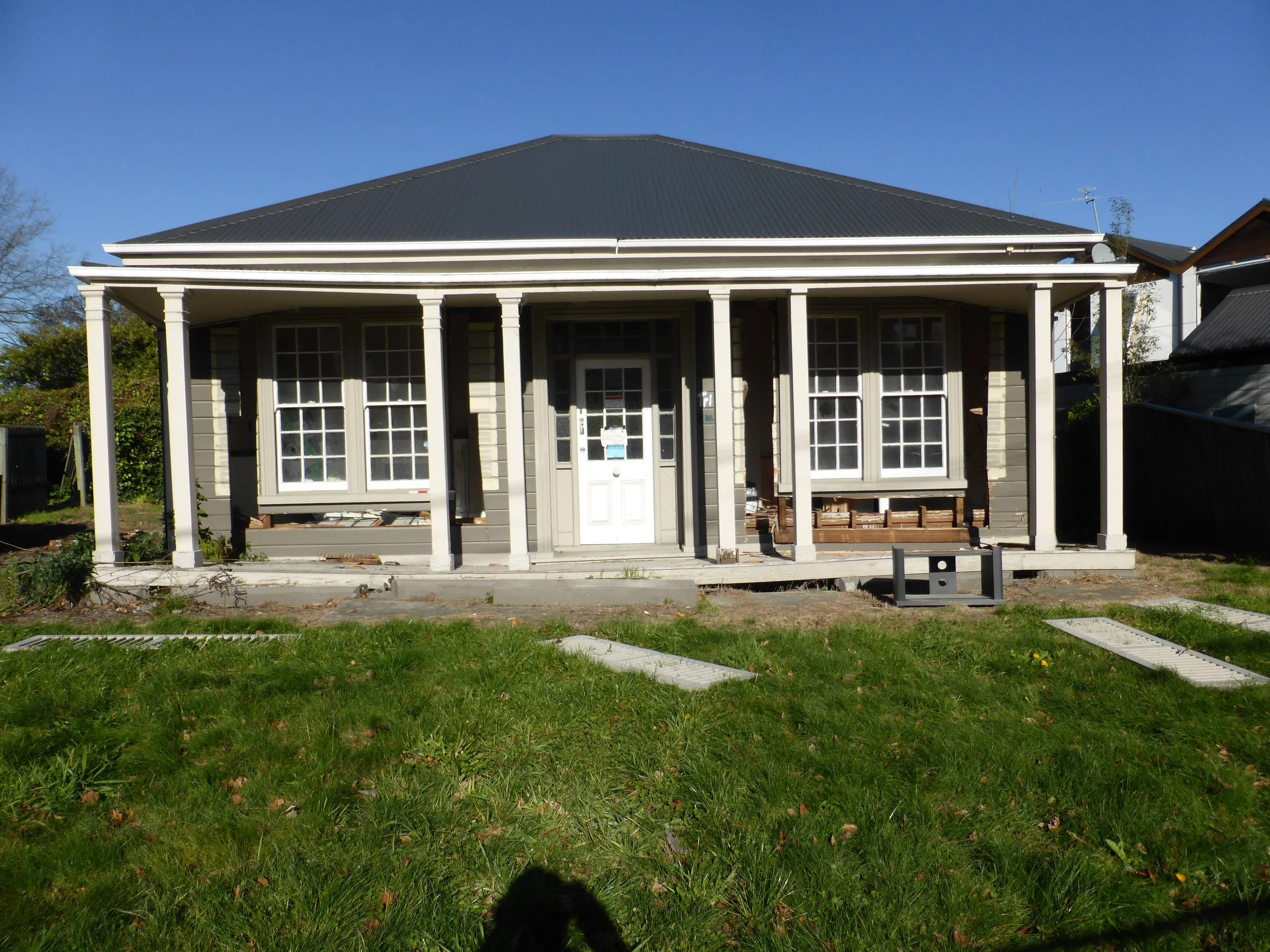 A single-storey weatherboard house with corrugated iron roof & veranda. Central front door with side and fanlights. Pairs of sash windows.