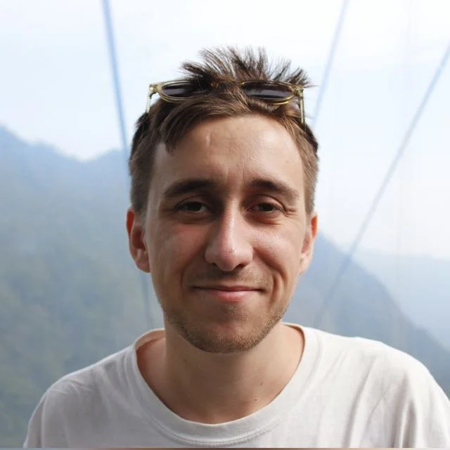 Close-up of a smiling young man with sunglasses on his head, outdoors with a view of foggy China huan-shan mountains in the background.