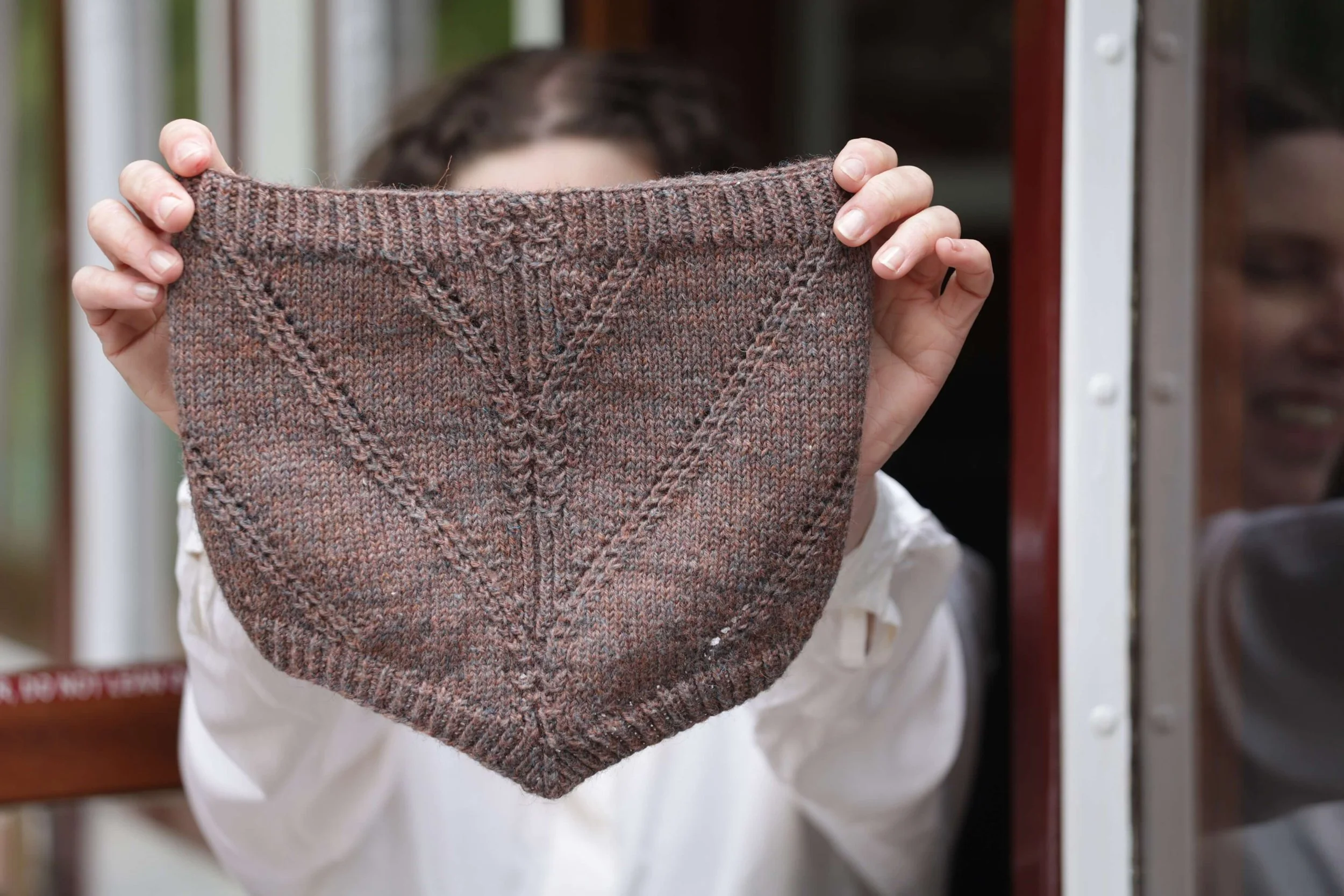 Someone holding up a finished object that they have just made from the knitting pattern in the John Arbon Textiles Annual knitting magazine