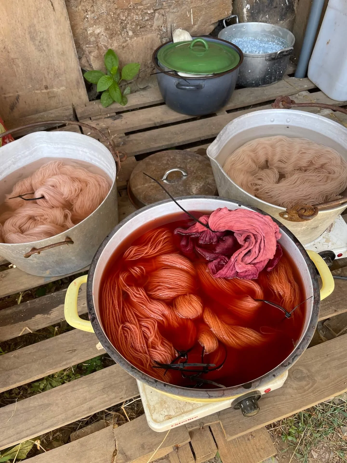 Several large pots with colorful fabric strips submerged in dye, used for yarn dyeing and dyeing of embroidery threads,, placed on a wooden surface.