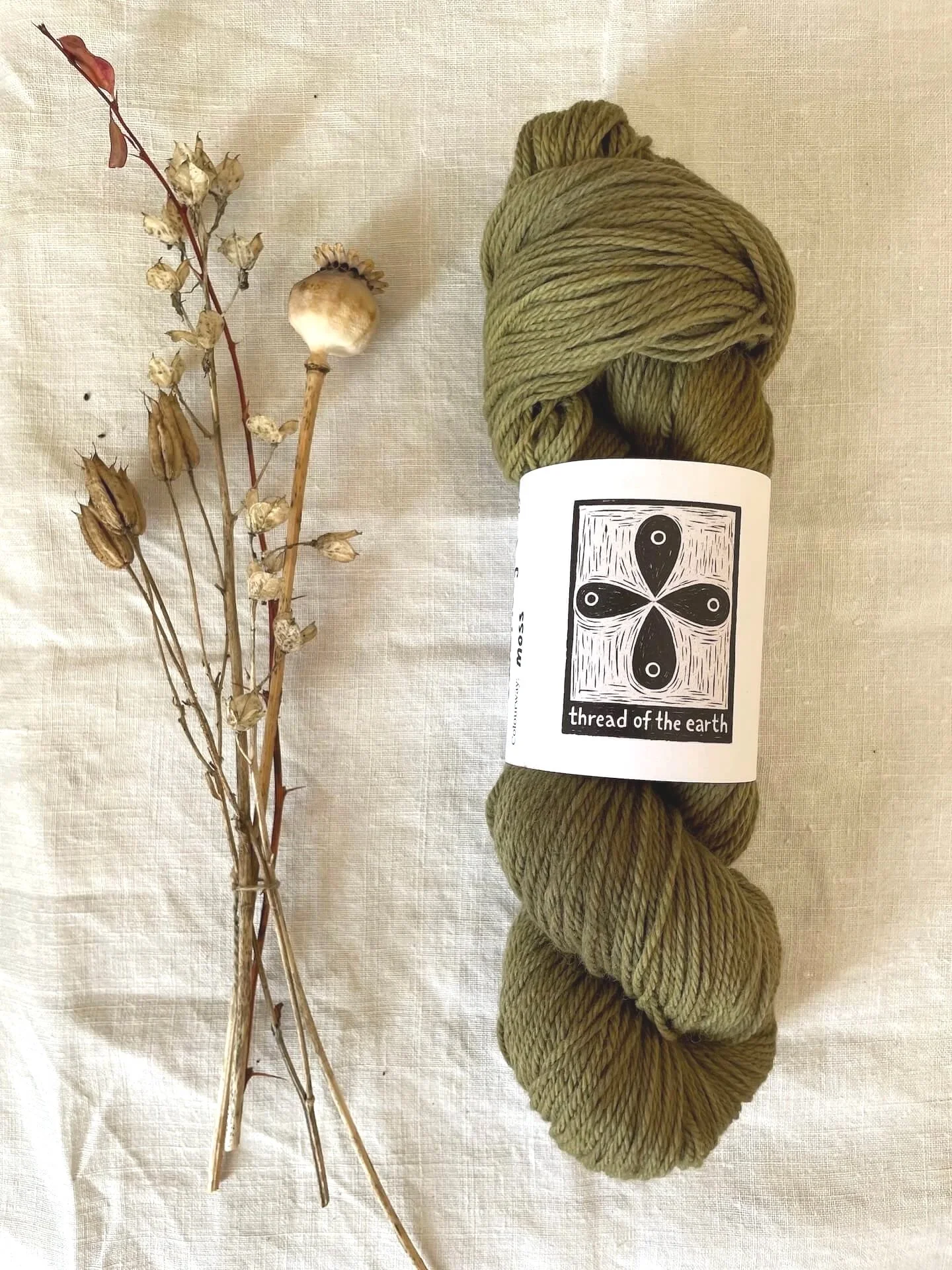 Naturally dyed skein of 100% merino wool on a linen table cloth with dried plant material.