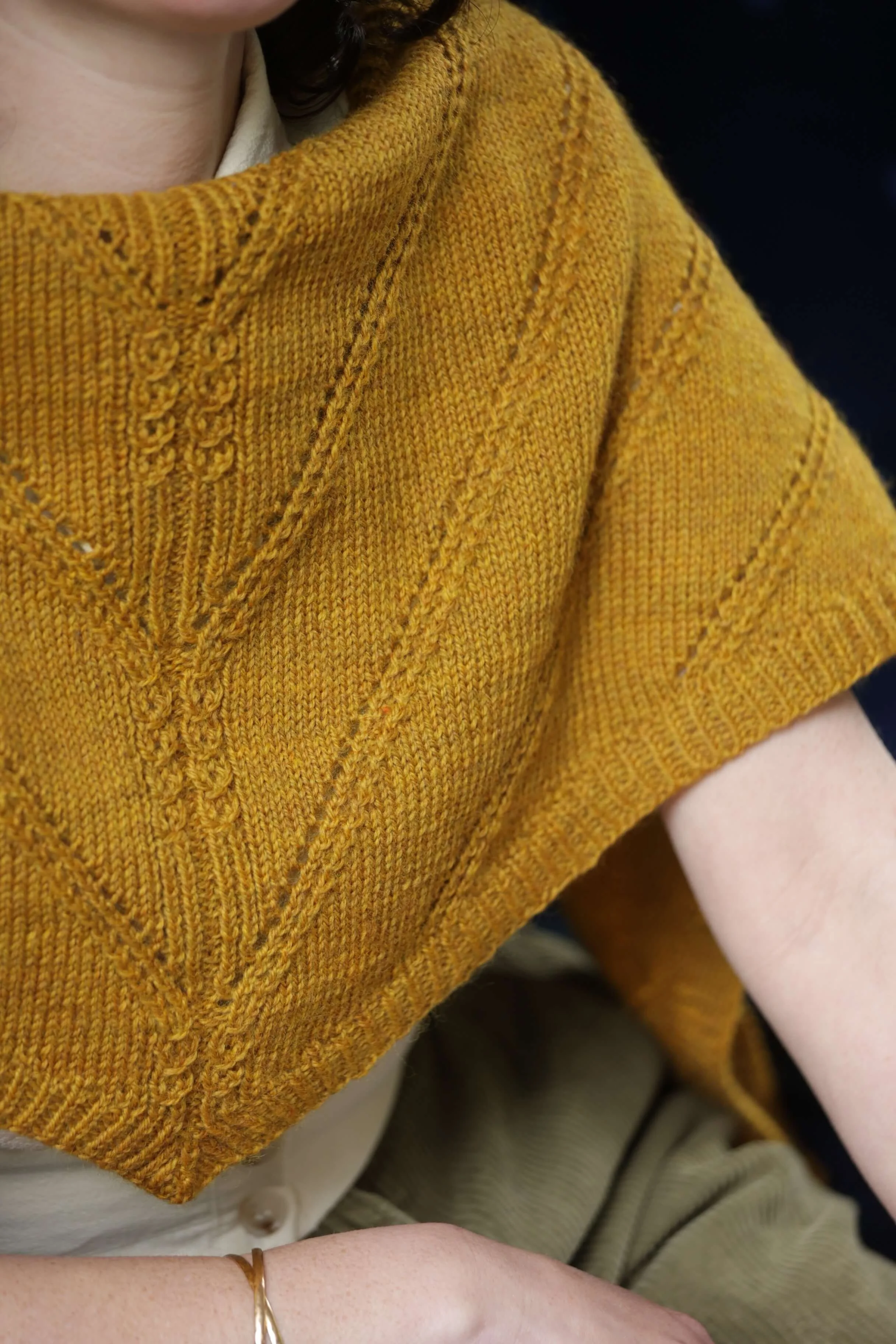 A woman wearing a hand knit woollen shawl in an original pattern with lace and cable details