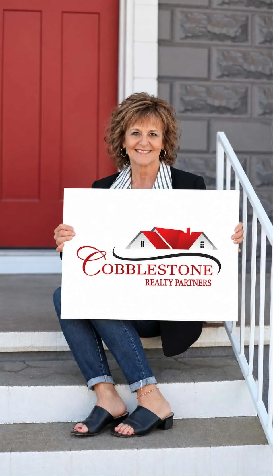 A woman sitting on steps holding a sign that reads "Cobblestone Realty Partners" with a house logo.