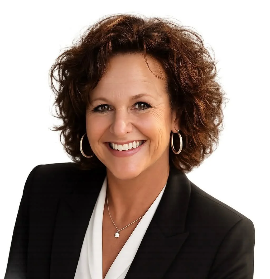 A smiling middle-aged woman with curly brown hair, wearing a black blazer, white blouse, hoop earrings, and a necklace with a small pendant, against a white background.