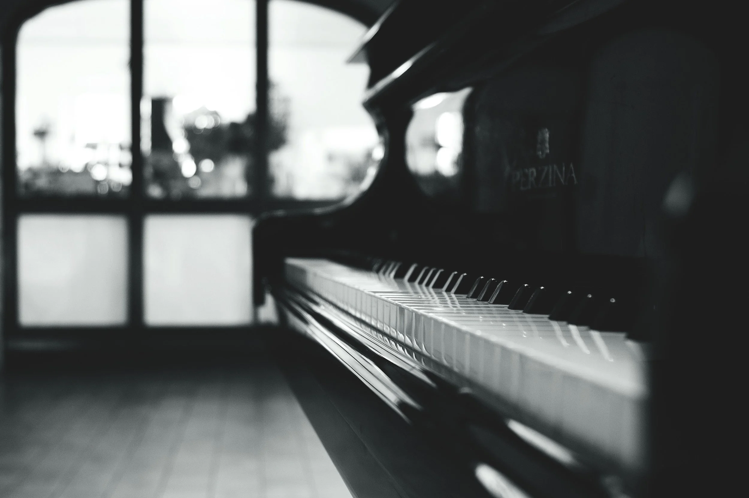 Close-up of a black upright piano keyboard with a blurred window in the background.