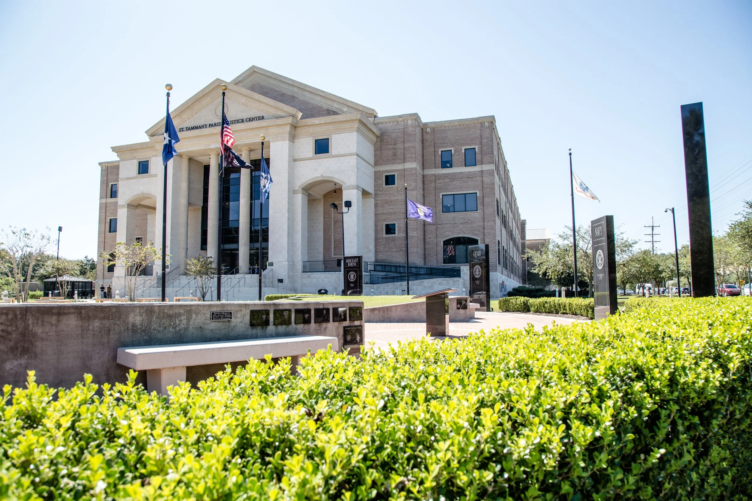 The exterior of the St. Tamnany Parish Justice Center building with flags flying in front and a pathway leading up to the entrance.