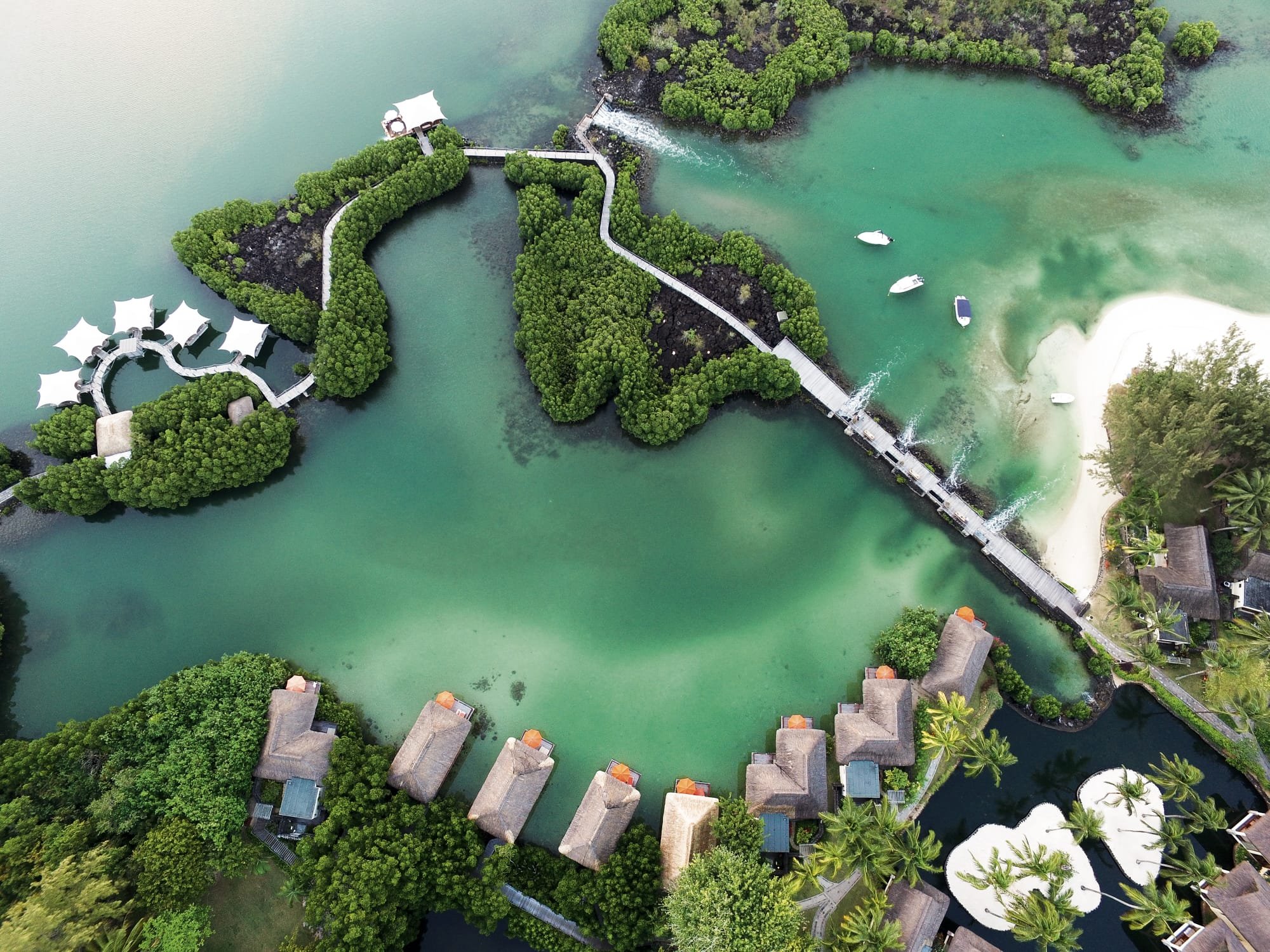 Luftaufnahme eines Mangrovenwaldes an der Küste mit Wasser und Booten, umgeben von Resorts und Palmendächern.