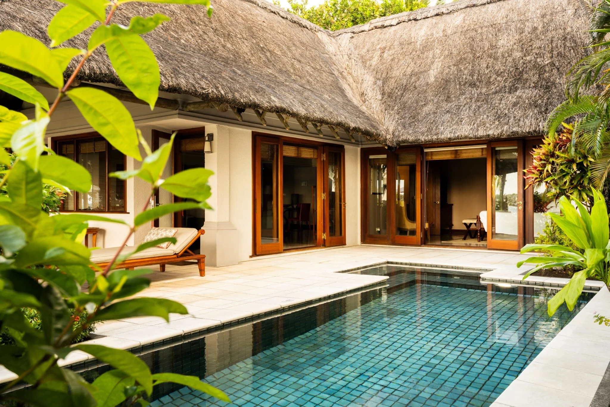 Ein Ferienhaus mit viel Holz und großen Fenstern, umgeben von Pflanzen, mit einem kleinen Pool im Vordergrund.