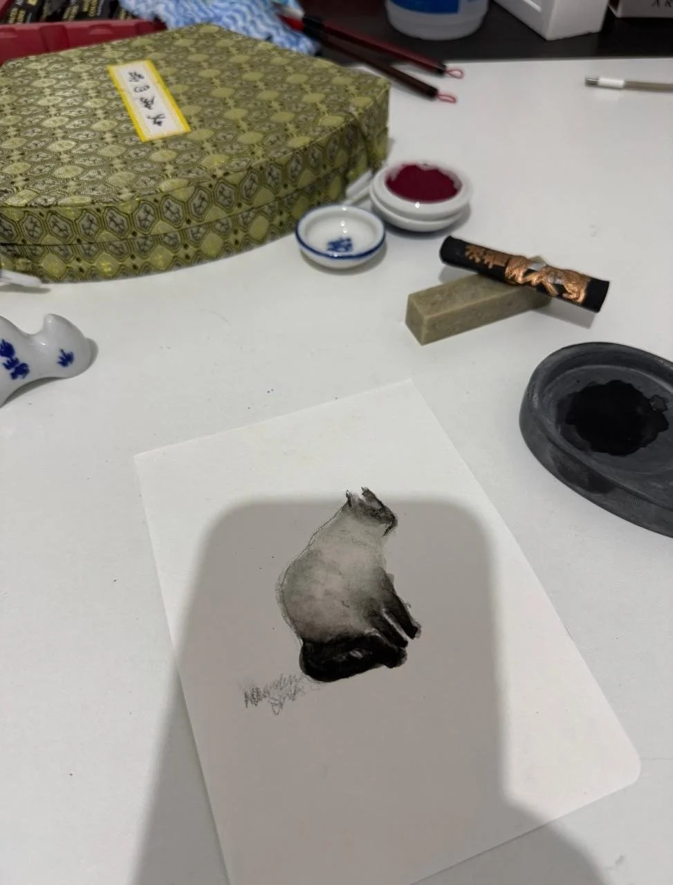 A watercolor painting of a dog's head on a white sheet of paper, surrounded by brushes, ink, and art supplies on a table.