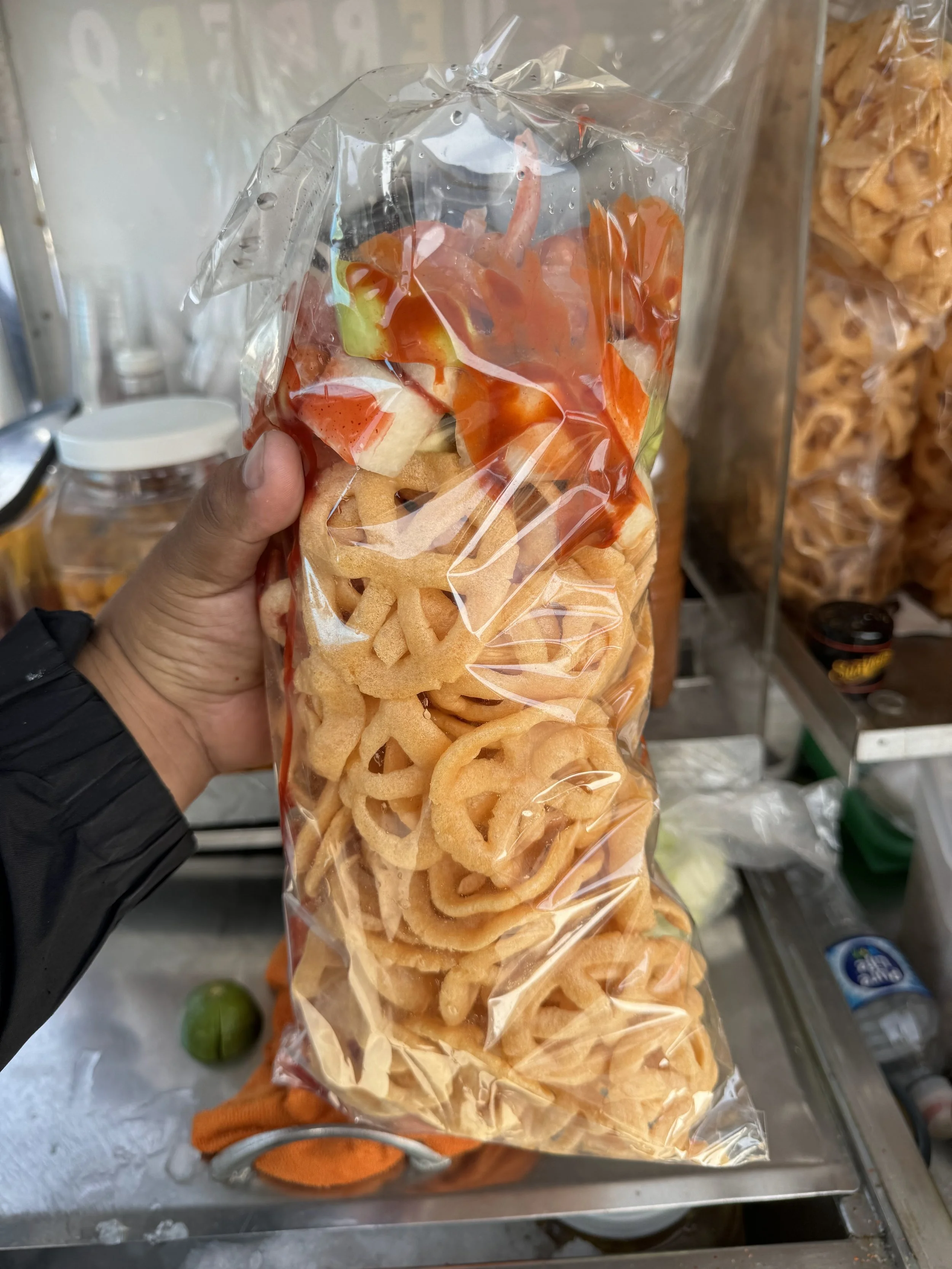 A hand holding a clear plastic bag filled with fried onion rings, with a store shelf in the background containing snacks.