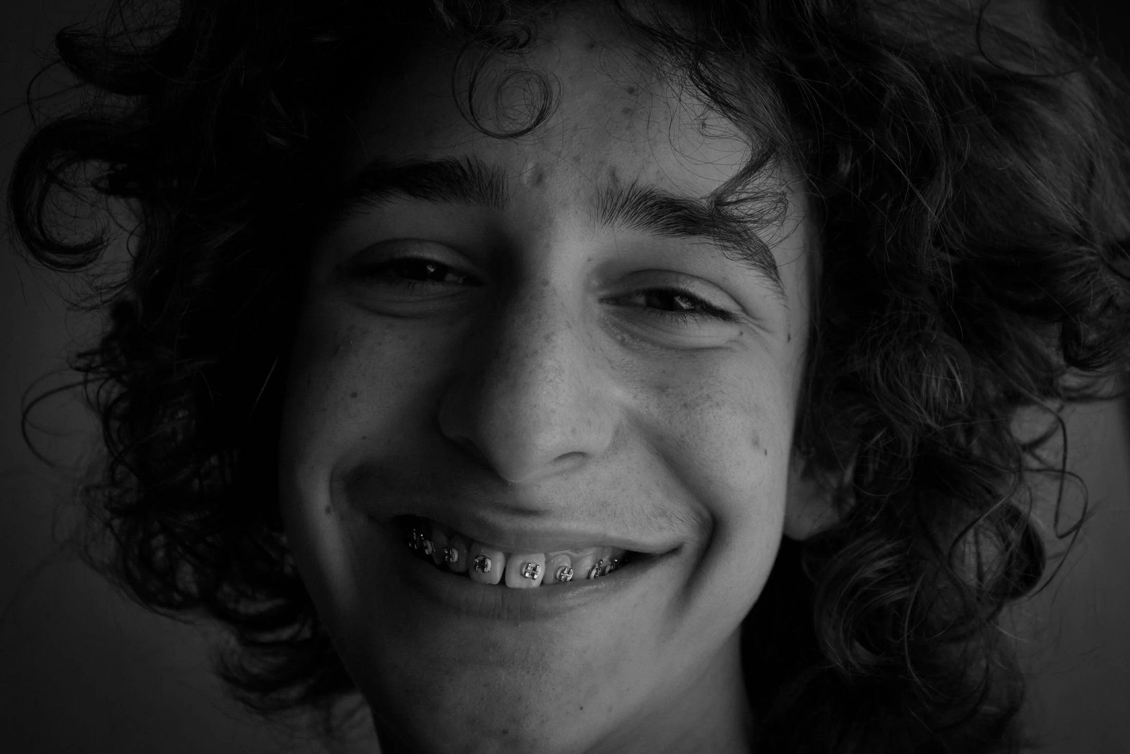 Close-up black and white photo of a woman with curly hair, smiling with their teeth visible.