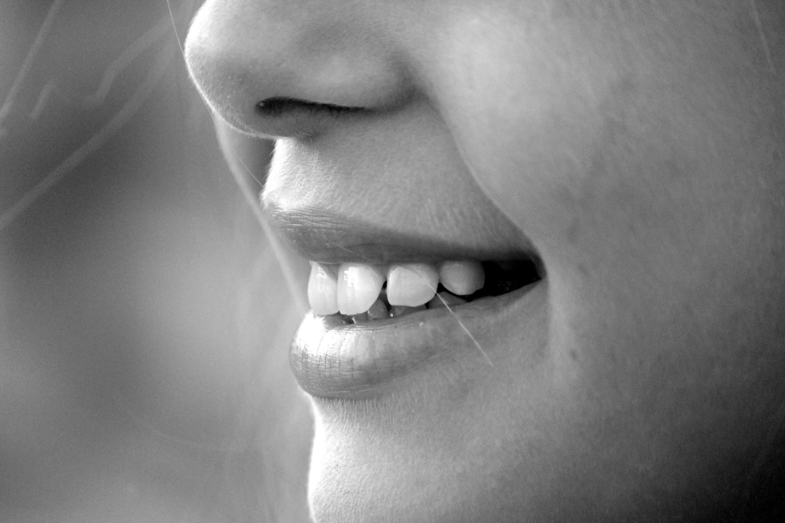 A close-up black-and-white image of a smiling person's face, showing their nose, mouth with visible teeth, and part of their chin.