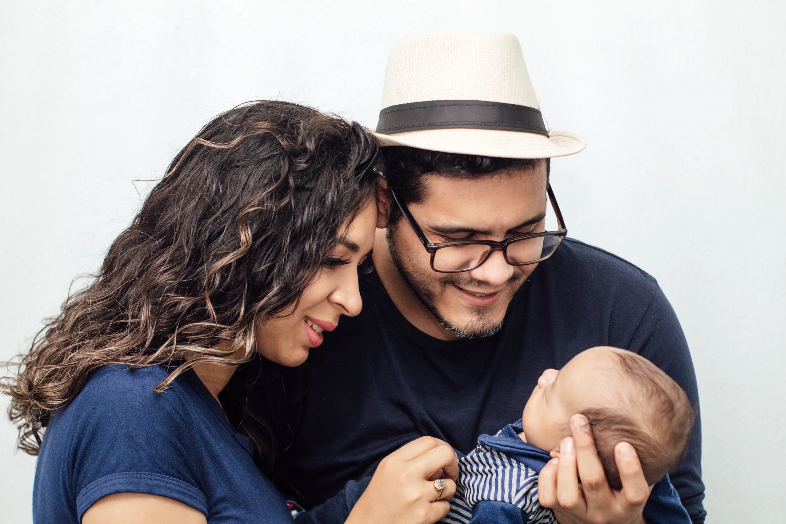 A woman and a man, both smiling, holding a baby, with the woman and man looking at something near the baby's hand.