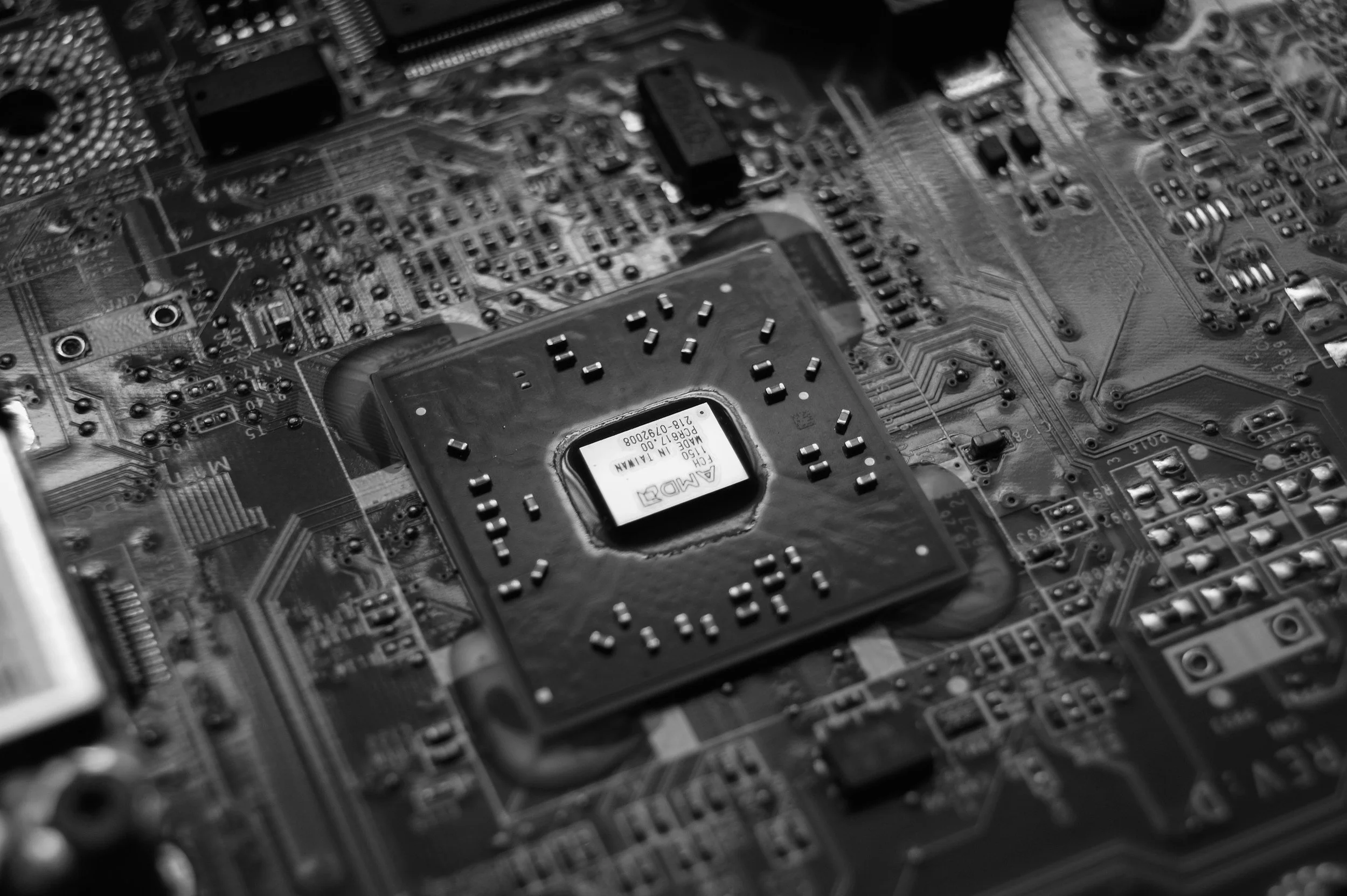 Close-up black and white photograph of a computer motherboard with various electronic components, chips, and circuitry.