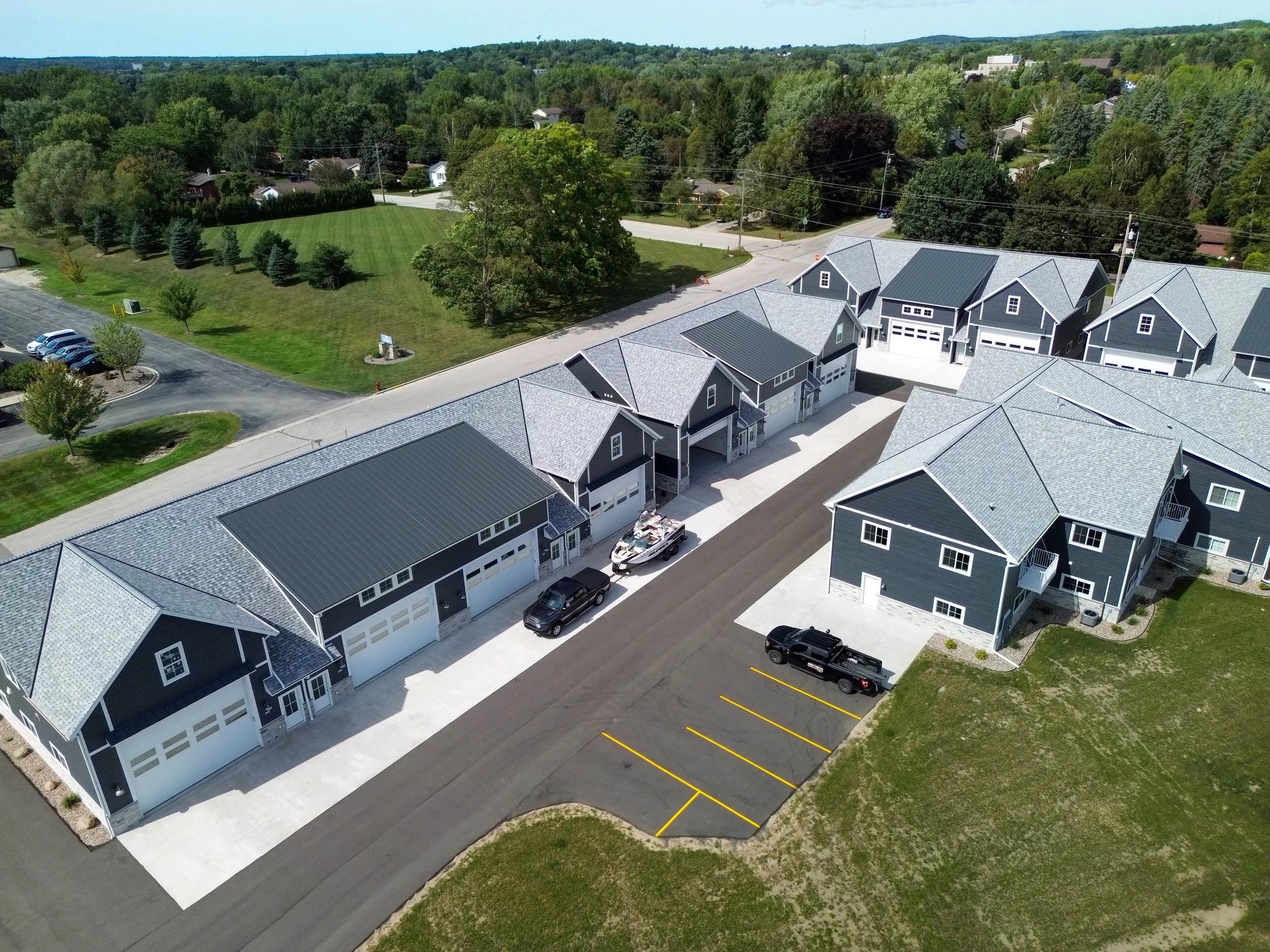 Aerial view of a residential neighborhood with new houses, a parking lot, and a grassy area surrounded by trees and greenery.