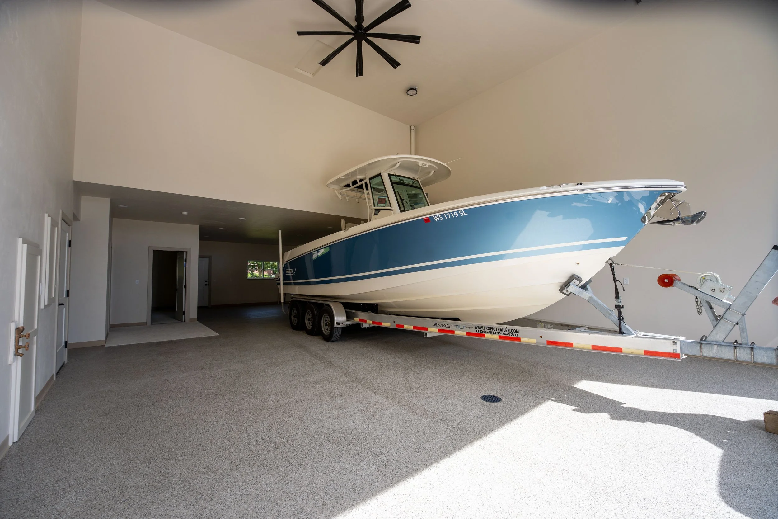 A large motorboat attached to a trailer inside a spacious, well-lit room with white walls and carpeted flooring.