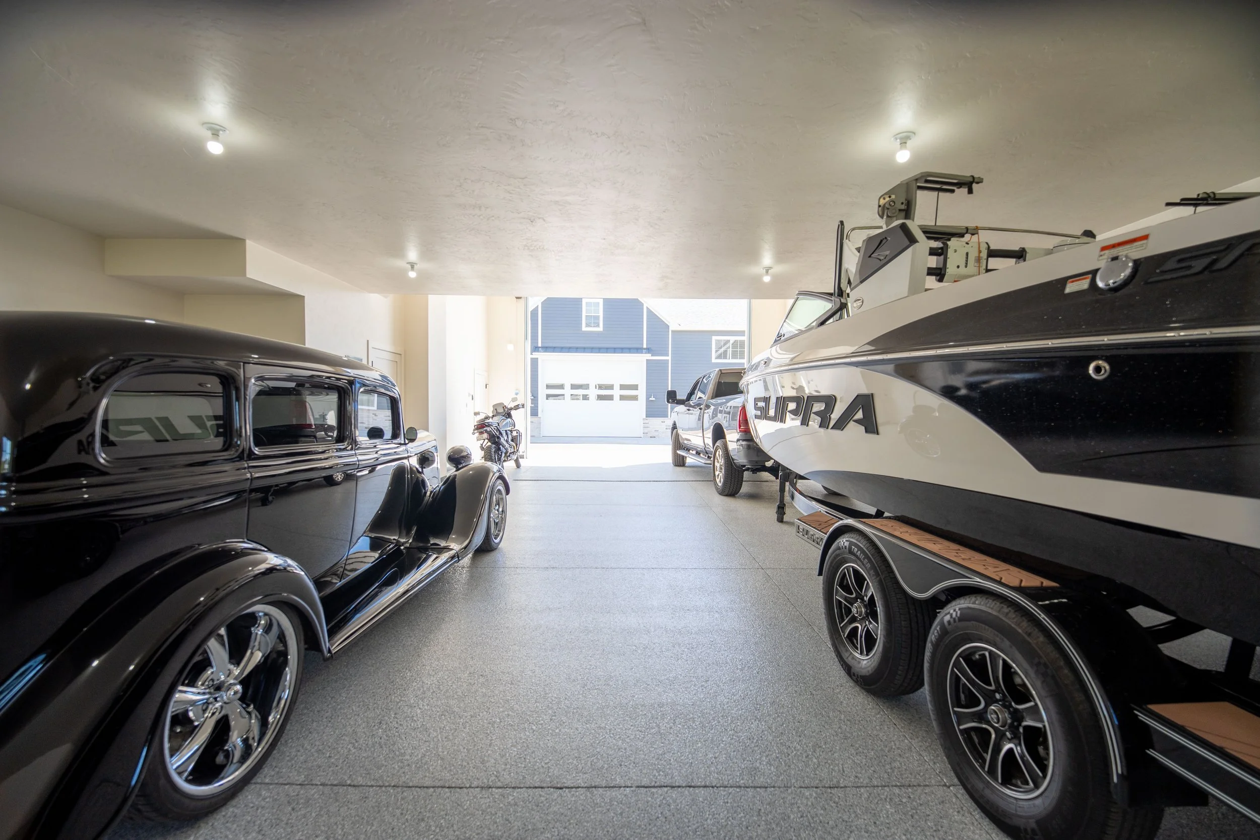 A garage with classic cars, a motorcycle, and a boat on a trailer.