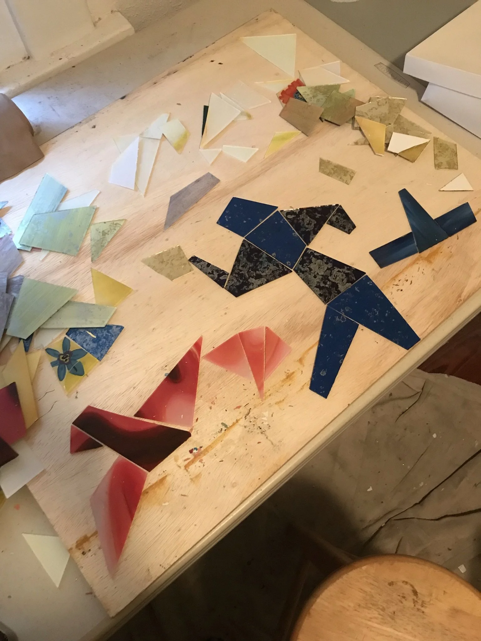 A wooden table with art supplies such as colored paper, paper triangles, and cut-out shapes.
