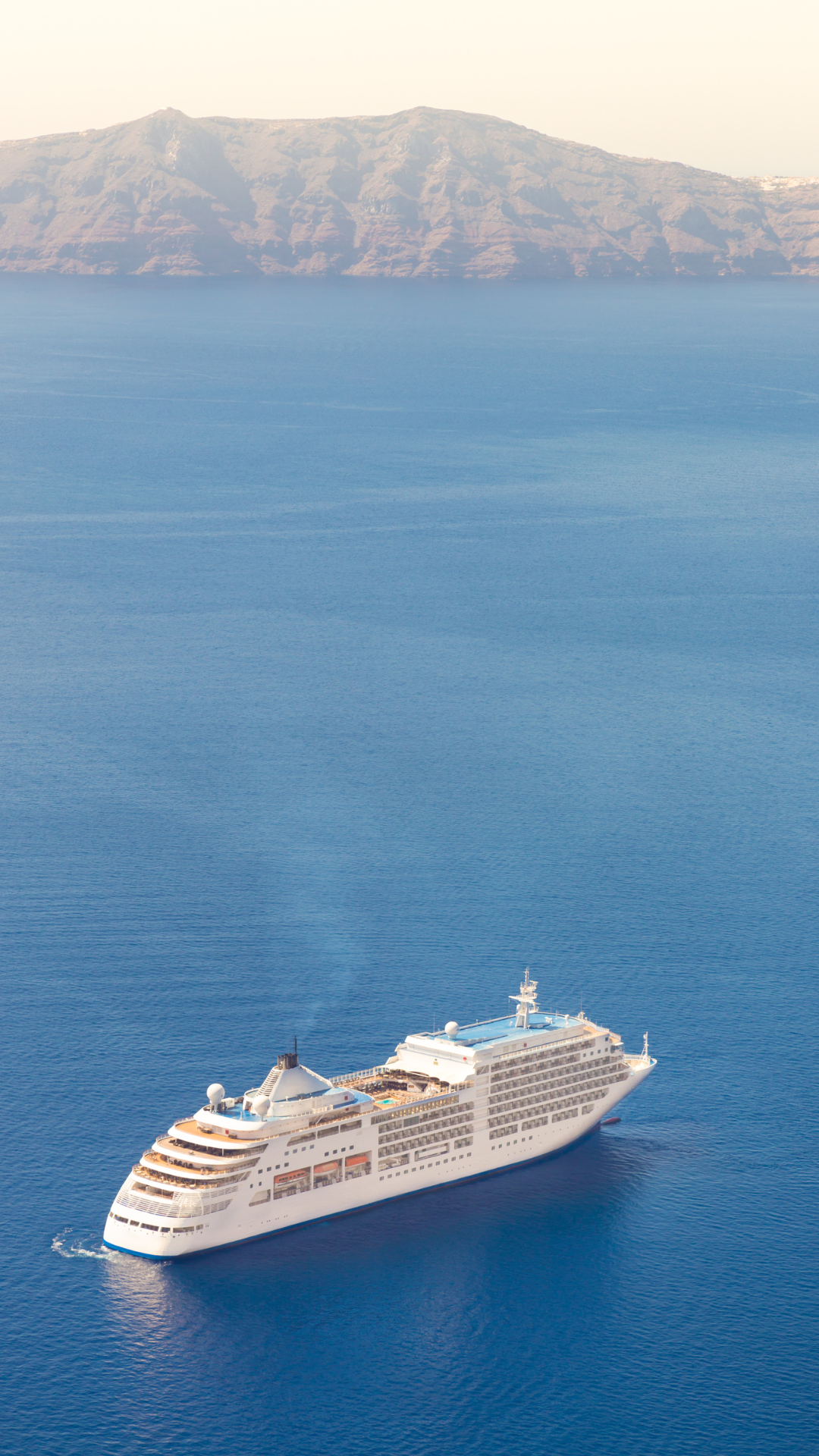 A cruise ship sailing in clear blue water with mountainous islands in the background.