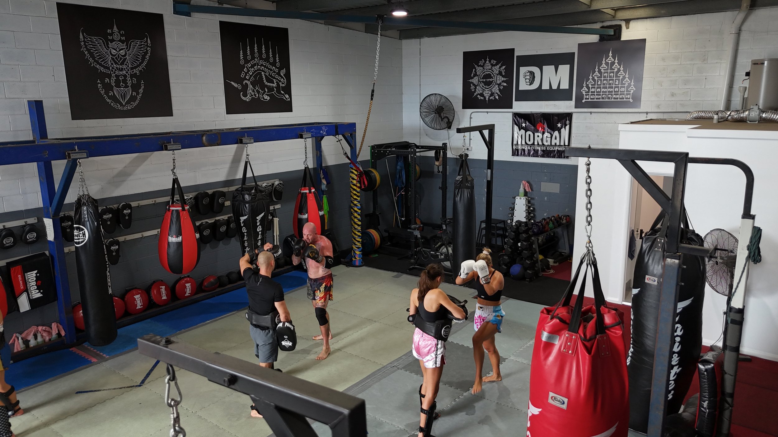 Training floor at DM Muay Thai & Fitness with heavy bags, pads and gloves on the wall, Tweed Heads South