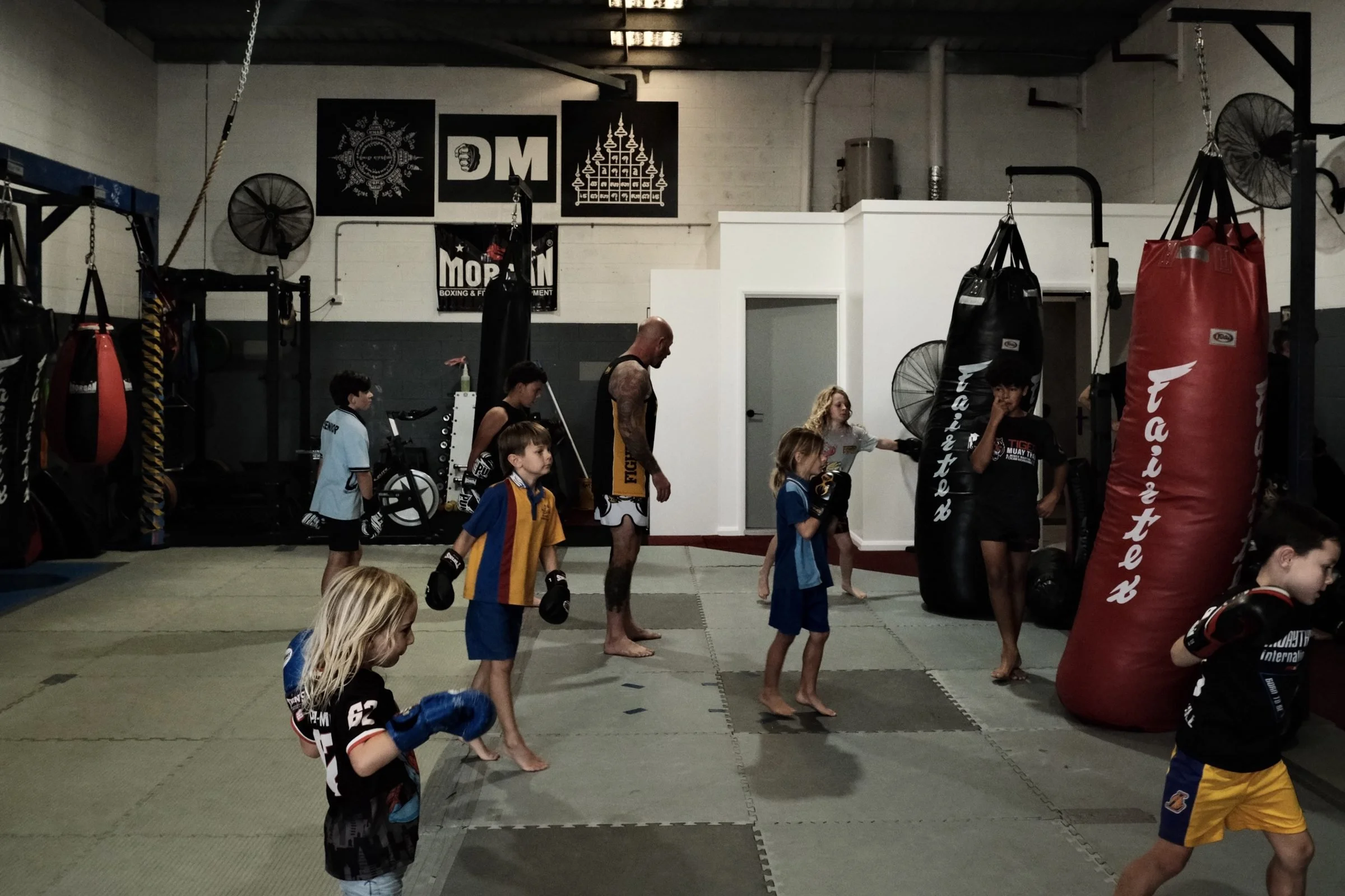 Kids working on the heavy bags with a coach during a Muay Thai kids class in Tweed Heads