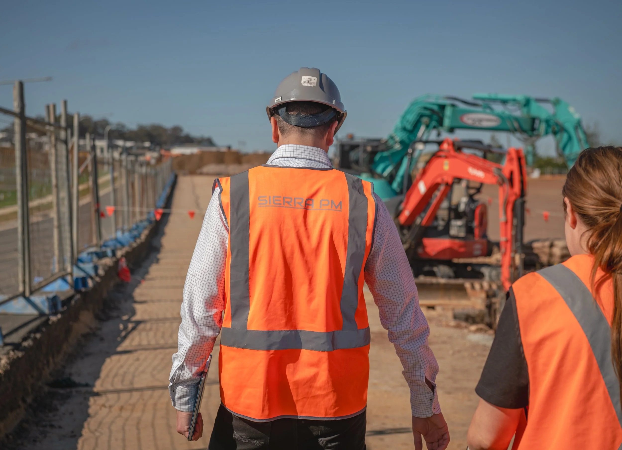 Construction workers wearing orange safety vests and helmets walking on a construction site with heavy machinery.