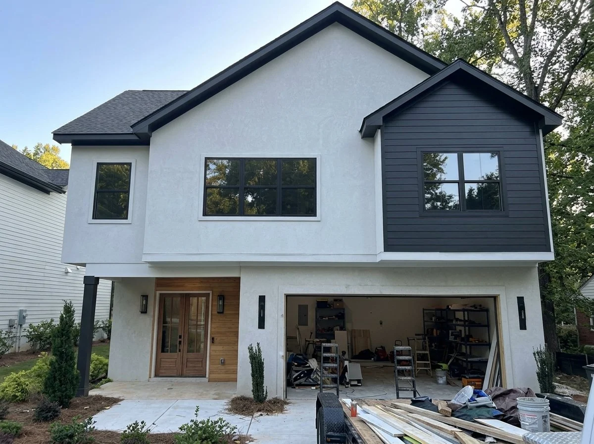 Newly constructed two-story house with modern design, white stucco exterior, black window frames, dark gray garage doors, and a black roof. The garage is open with tools and equipment visible inside.