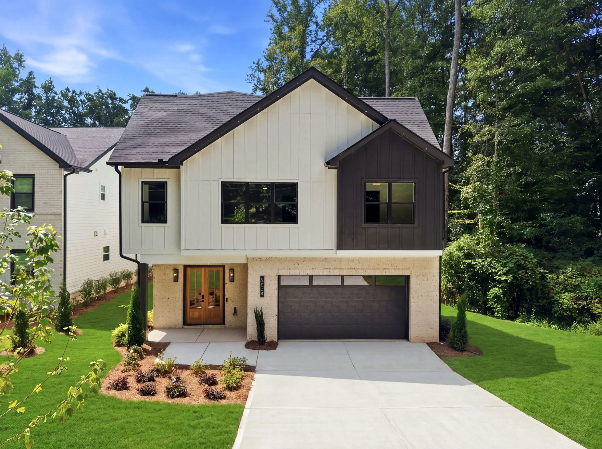A modern two-story house with a landscaped front yard, a driveway leading to a garage, and a two-tone exterior with beige and dark brown siding, surrounded by mature trees.