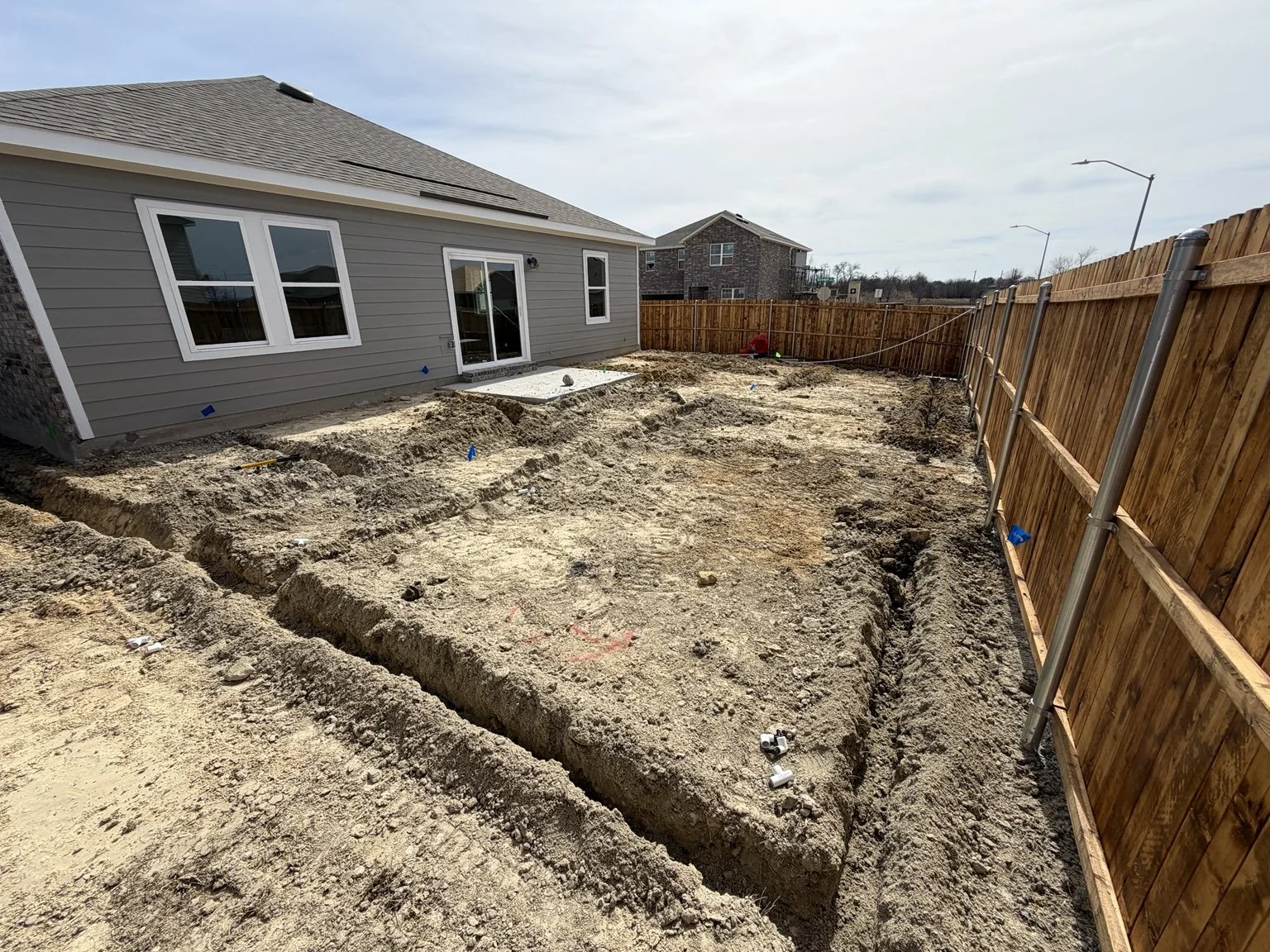 Residential irrigation installation — backyard trenching and marked sprinkler locations.