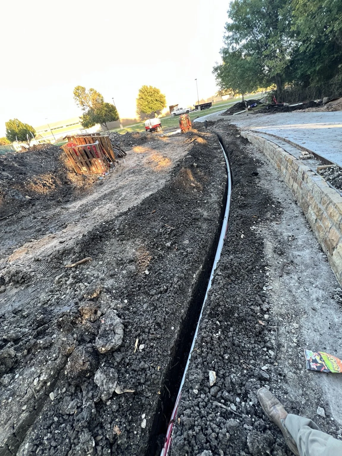 Trail irrigation installation — trenching and pipework along the curved wall.