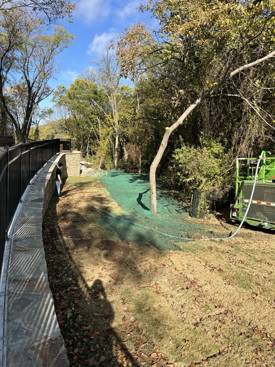 Slope restoration — green erosion-control treatment beside the stone wall.