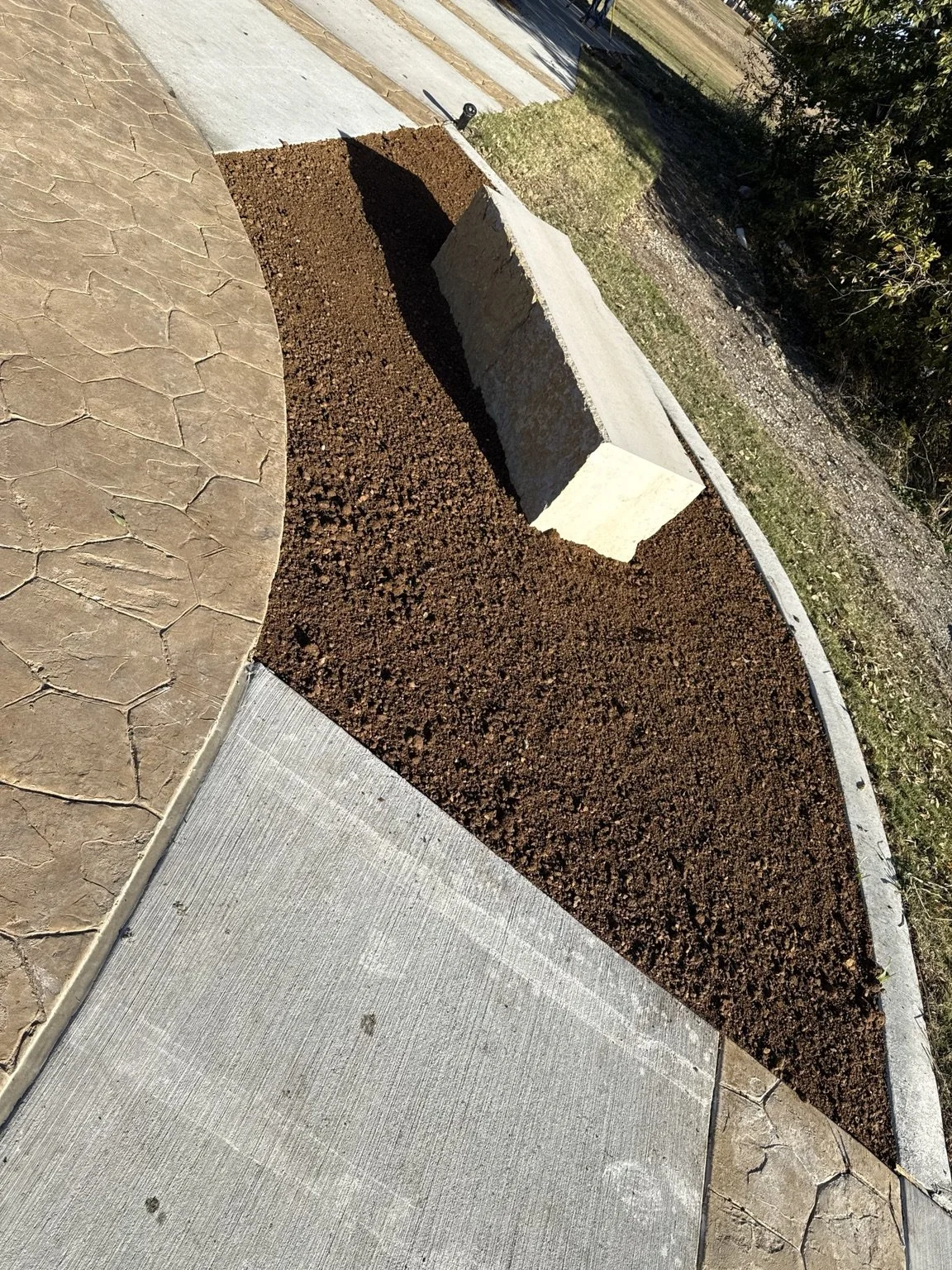 Trail-side site preparation — graded planting area around a stone bench.
