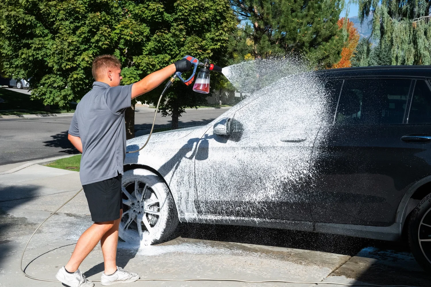 Detailer foaming an SUV at the curb on a residential street