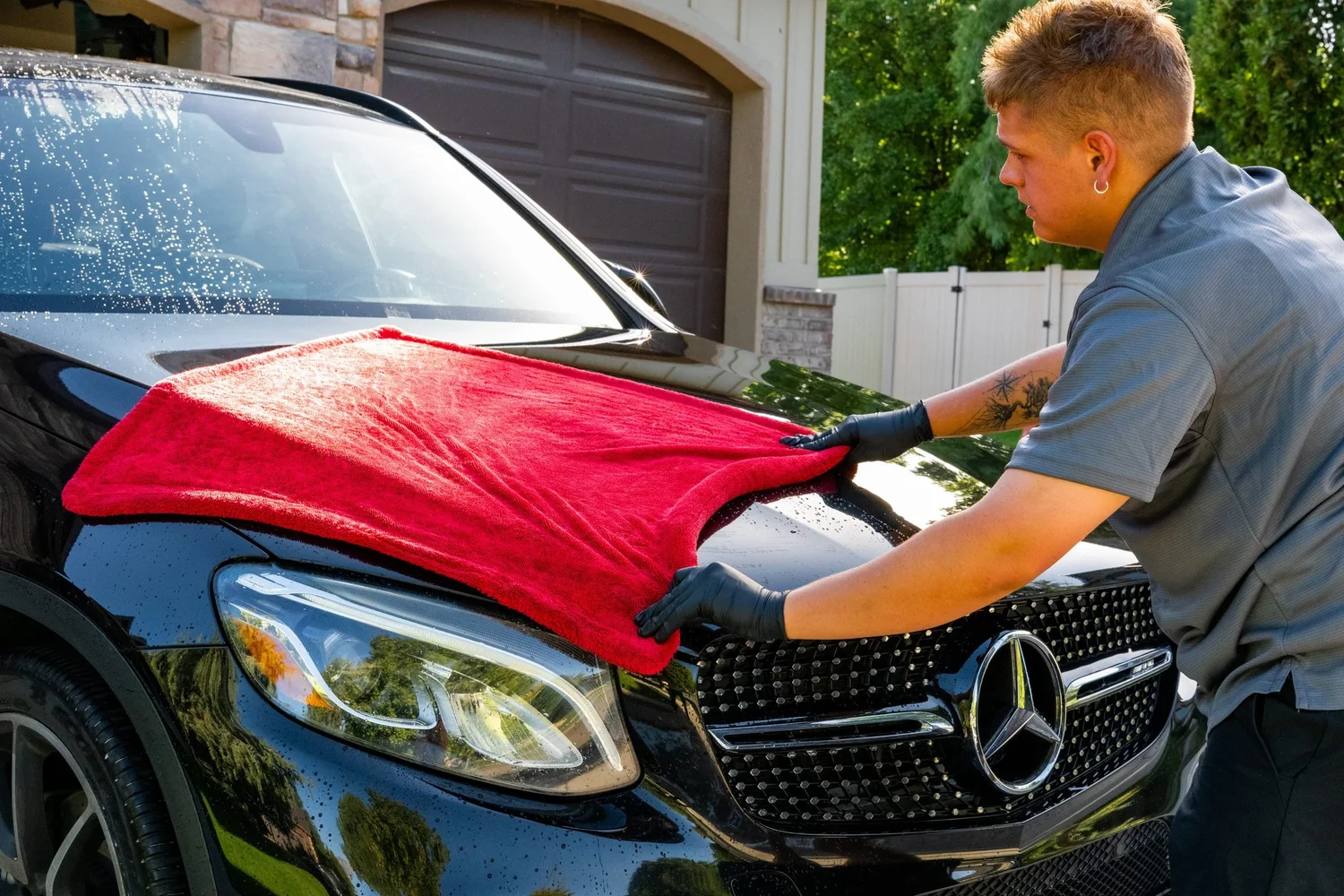 Detailer drying a black SUV hood with a red microfiber towel