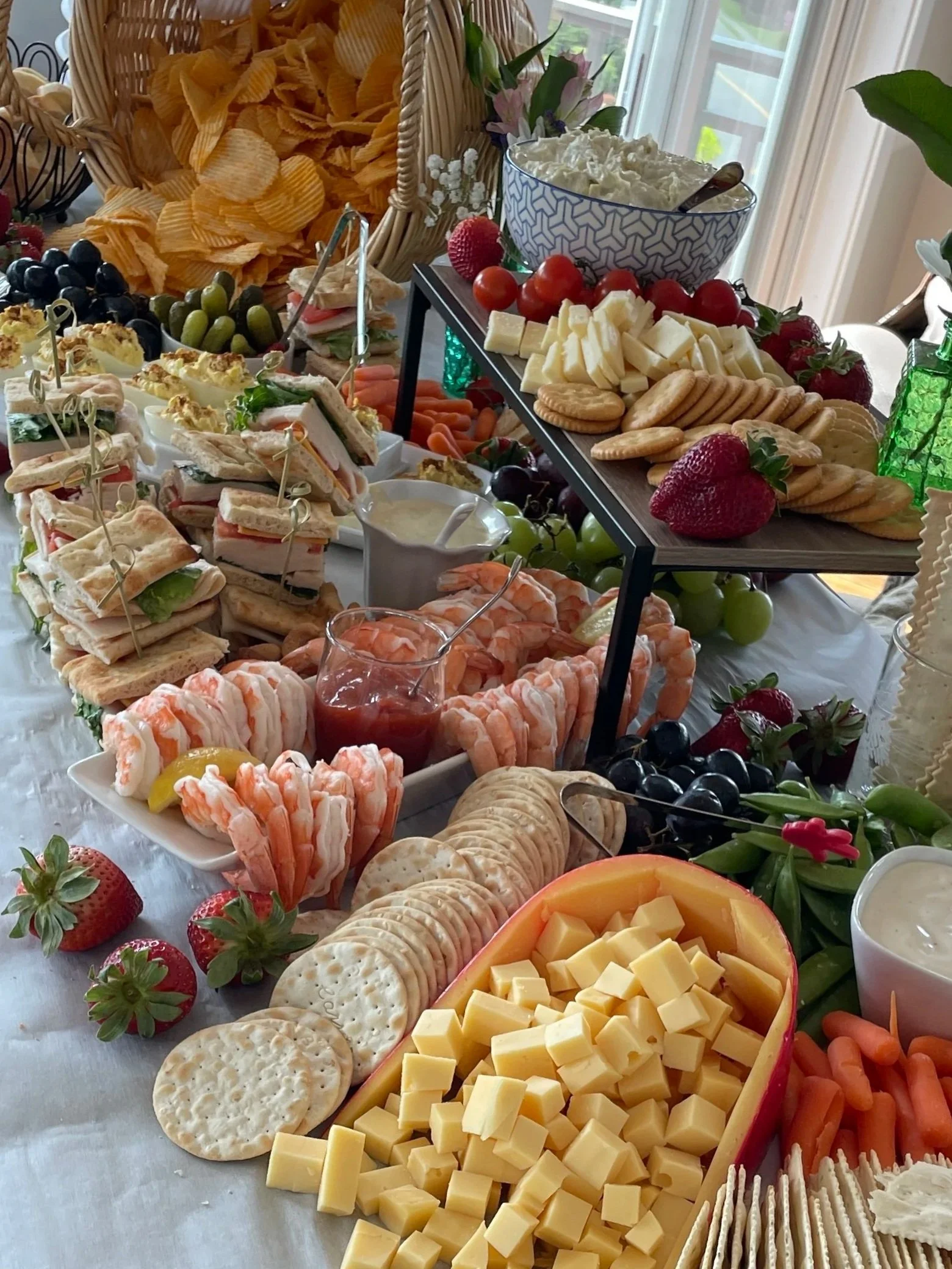 A cheese and charcuterie platter with grapes, strawberries, crackers, shrimp, and various cheeses, garnished with flowers.