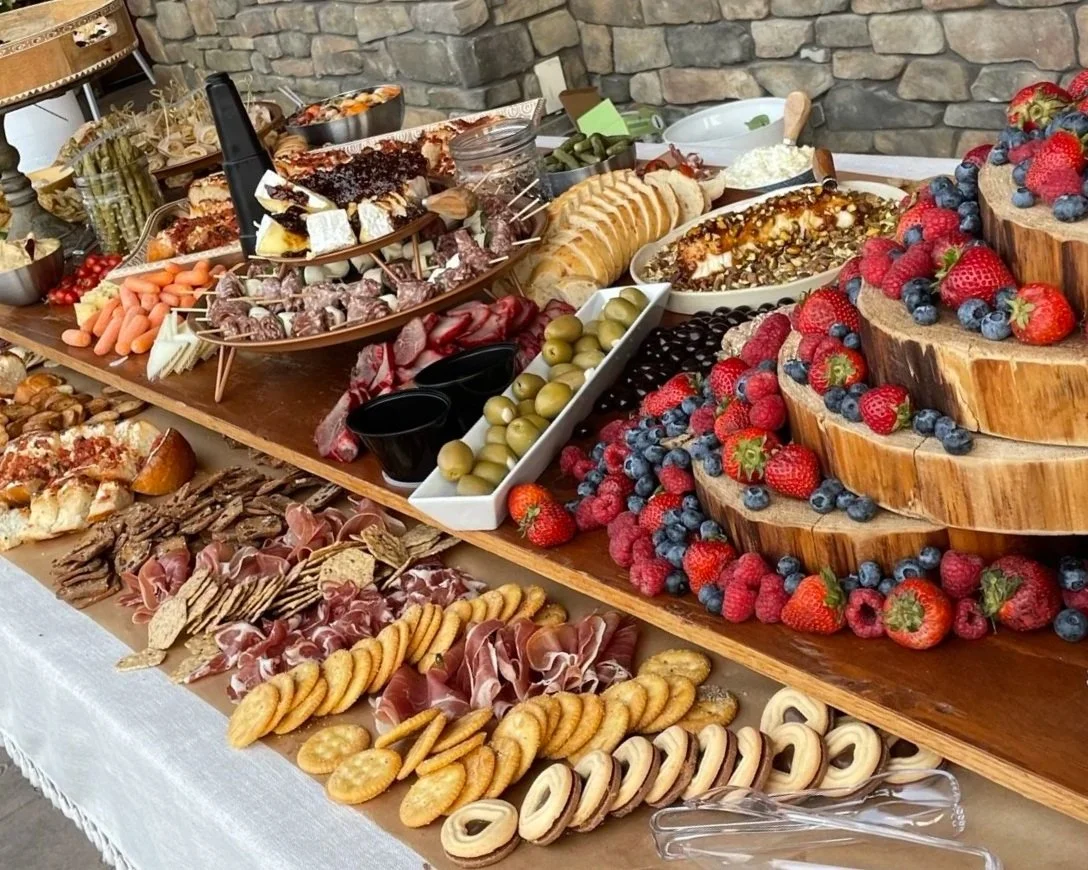 A rustic buffet table with an assortment of desserts, cheeses, olives, meats, fruits, and crackers, including strawberries, blueberries, raspberries, slices of bread, and various sweets.