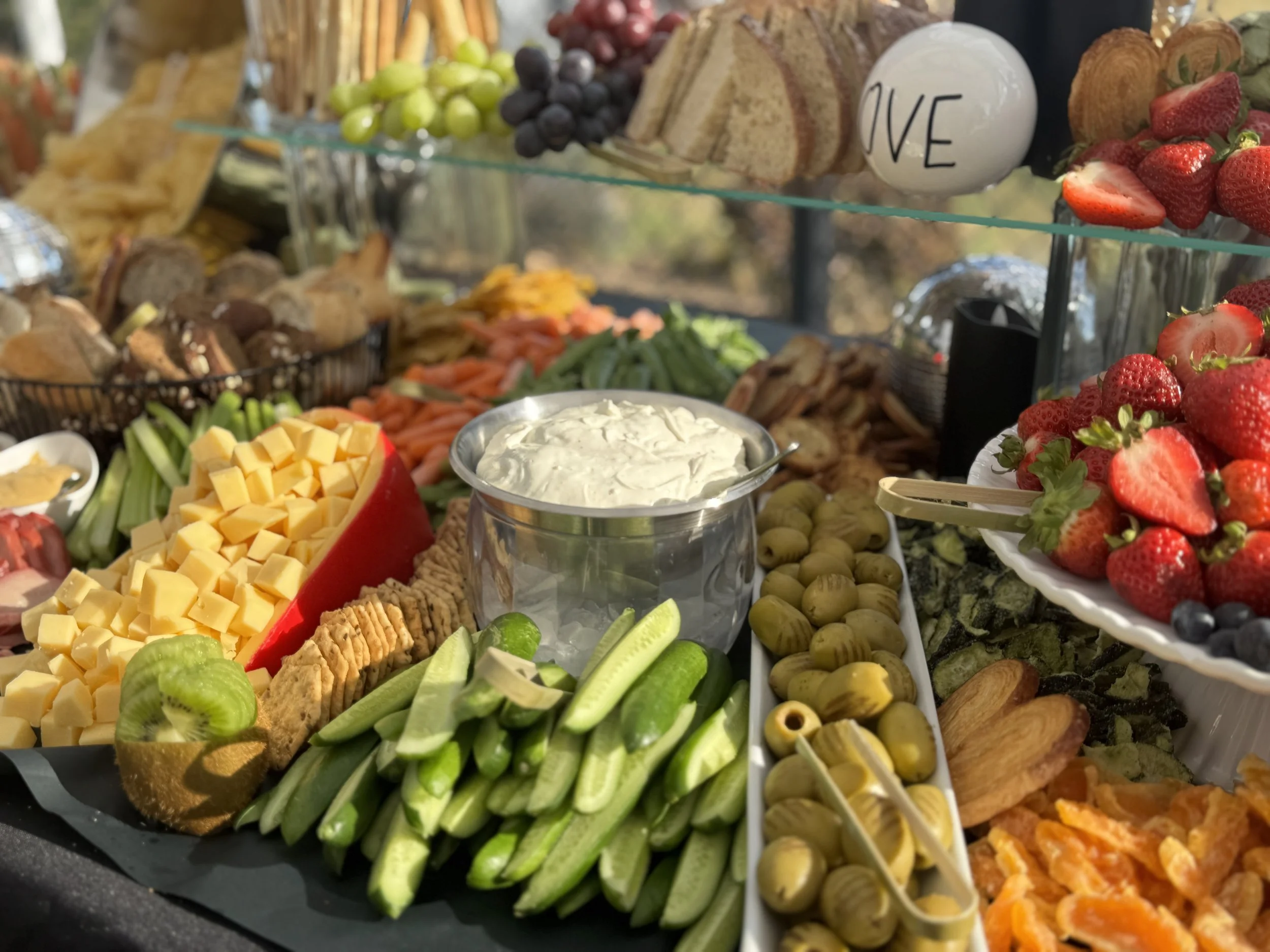 A variety of fresh fruits, vegetables, cheeses, and dips arranged on a platter, with a decorative white ball that has the word 'LOVE' written on it.