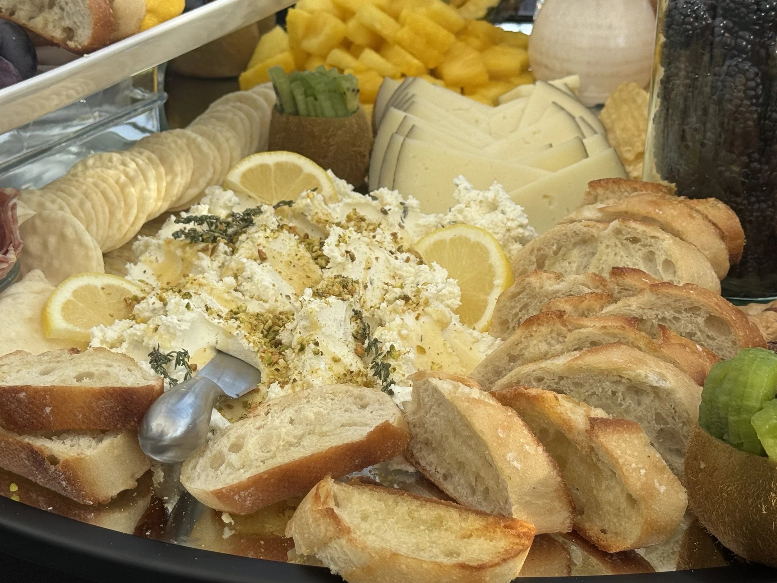 Assorted cheeses, sliced bread, lemon wedges, crackers, and grapes on a platter at a party or buffet.