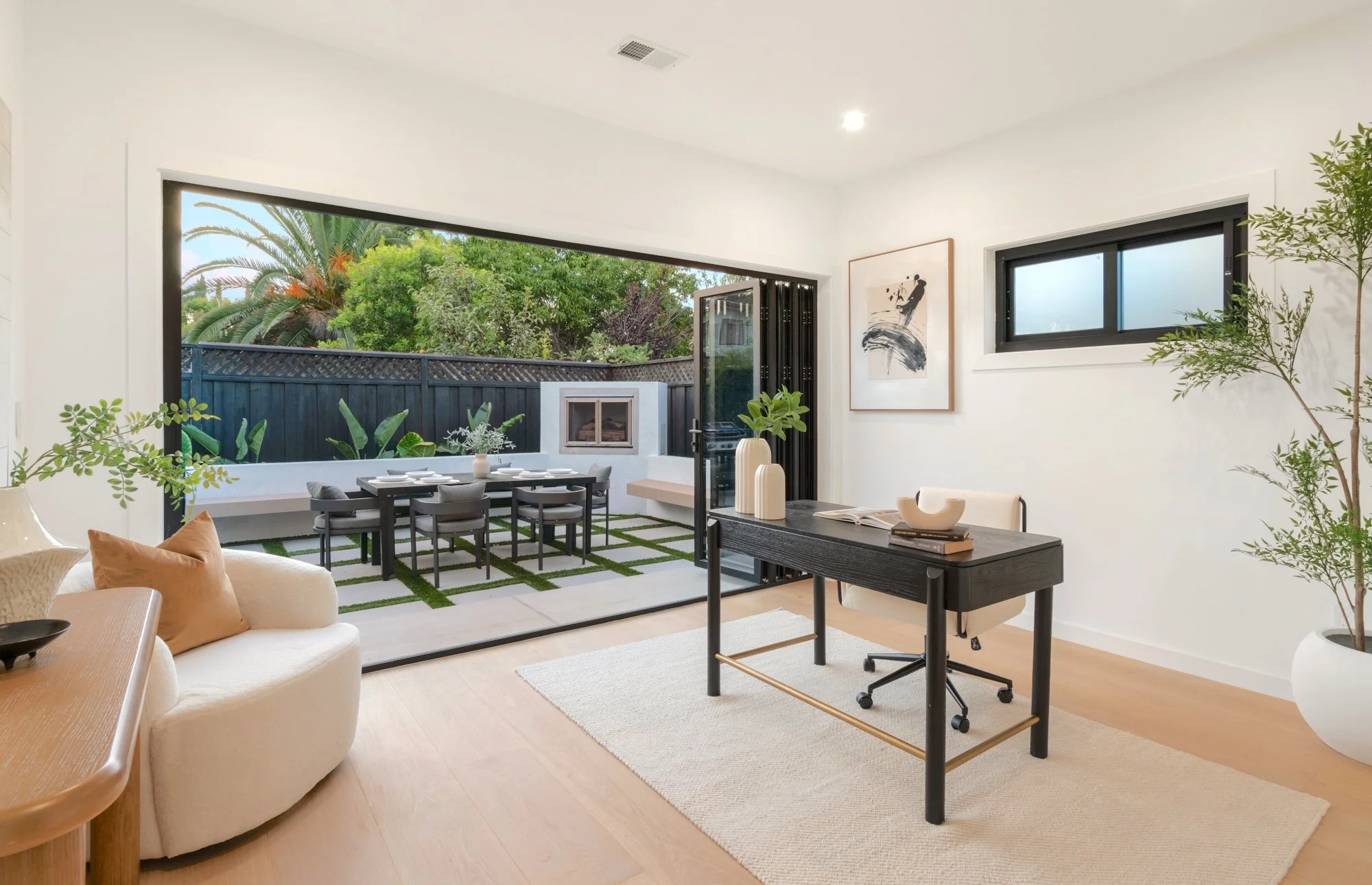 Interior view of a modern living room with an open door leading to a patio with outdoor furniture, greenery, and trees.