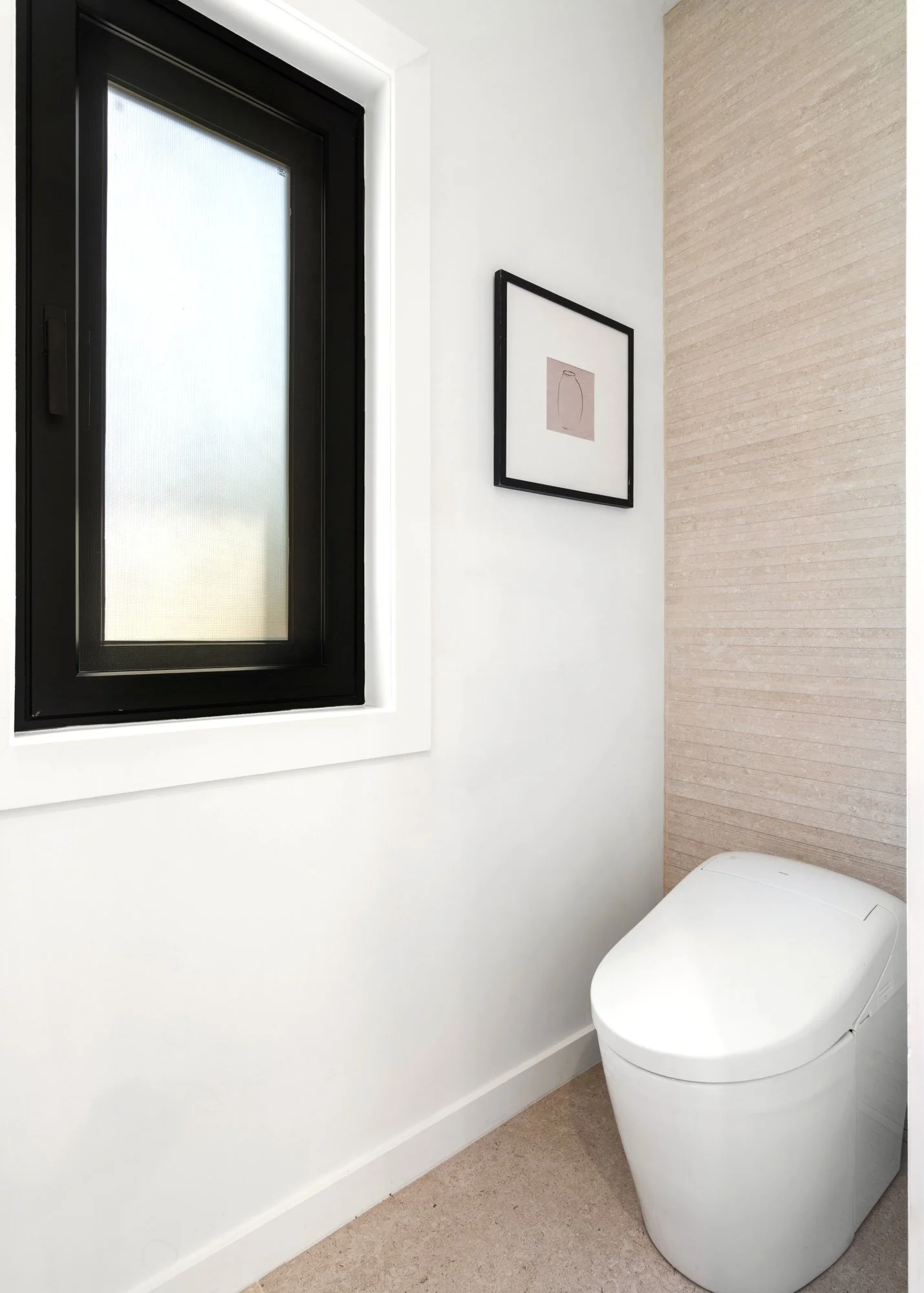 Modern bathroom with a sleek, white toilet, a frosted window with a black frame, and minimalistic artwork on the wall.