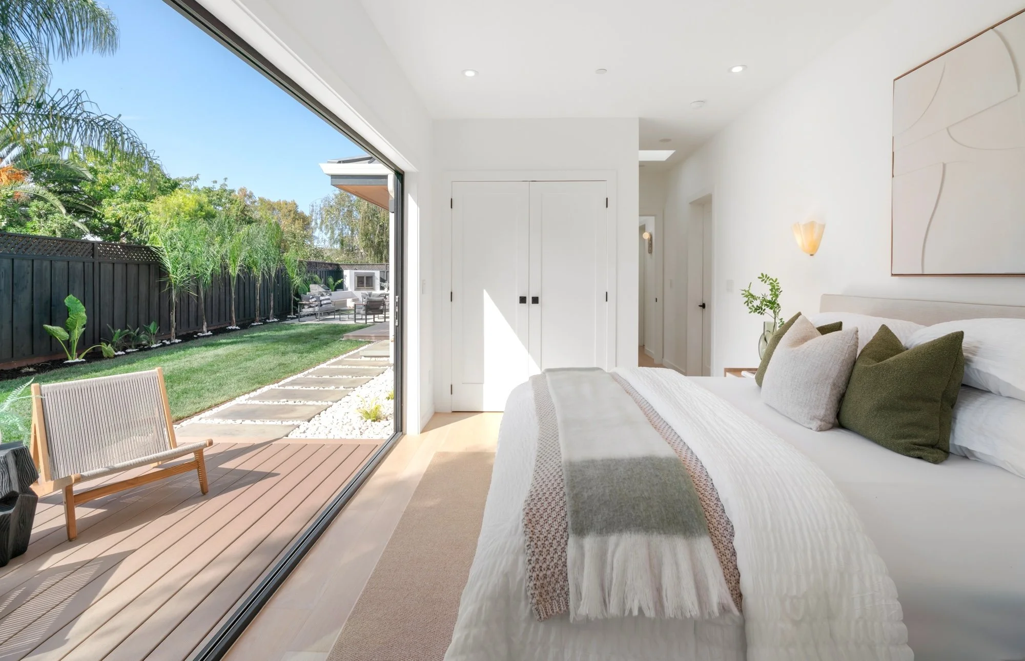 Bedroom with a large sliding glass door opening to a backyard patio with outdoor seating, lush green grass, and trees.