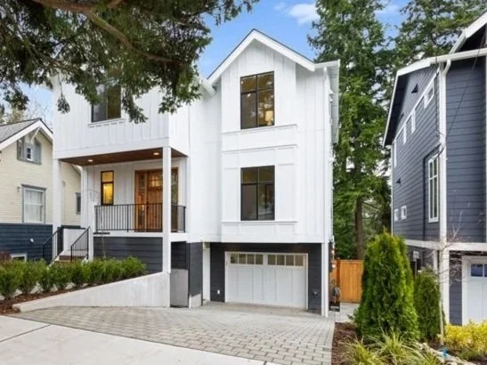 Modern three-story white house with a two-car garage, front porch, and landscaped yard in a suburban neighborhood.