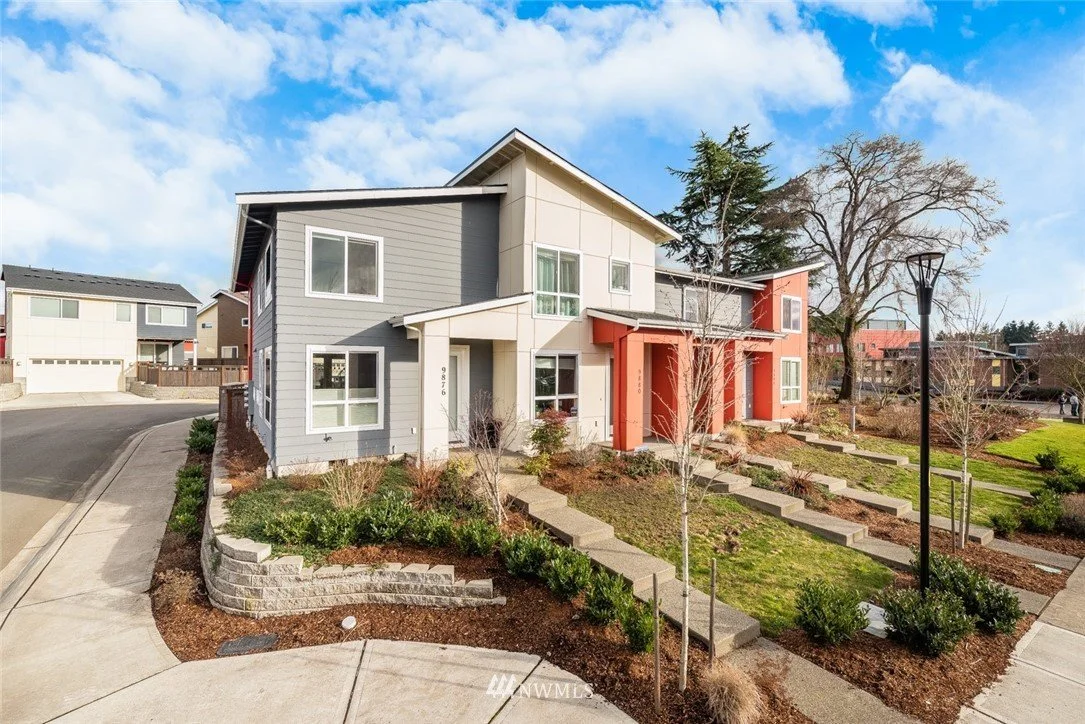 Modern colorful two-story residential building with landscaped front yard and a sidewalk.