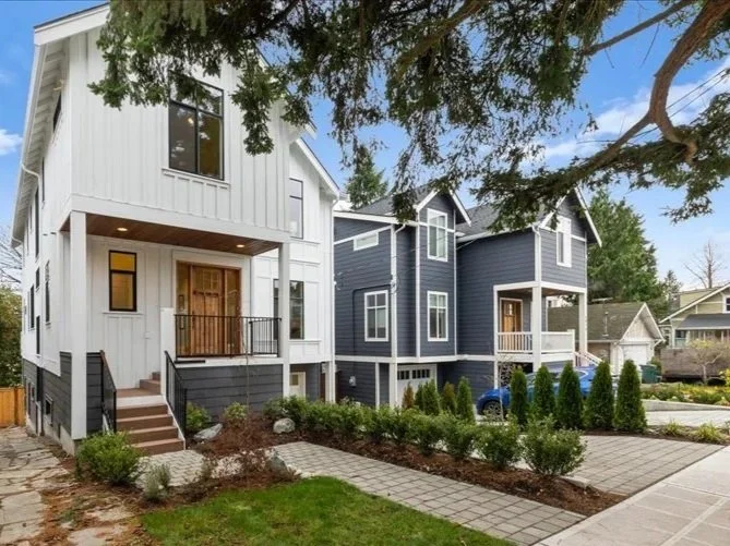Newly built modern two-story houses in a suburban neighborhood, with landscaped front yards and trees.