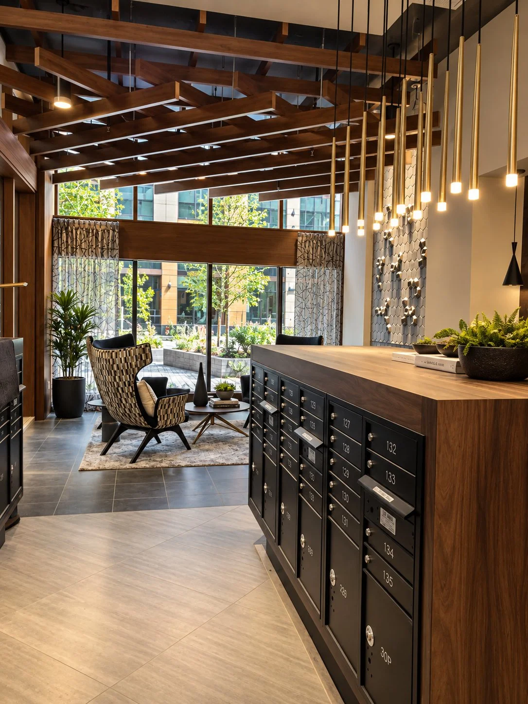 Indoor lounge area with modern decor, black mailboxes, a wooden countertop, and seating area by large windows with plants outside.