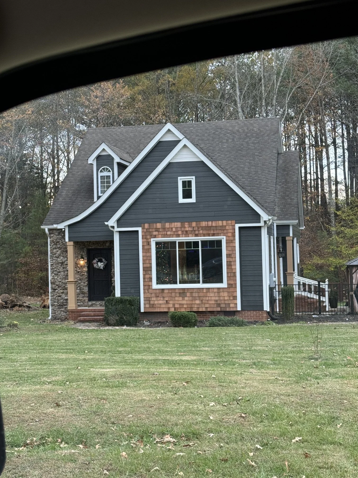 Photo of a house with dark blue siding, a brick front, and a gabled roof, viewed from a front yard with grass and trees in the background.