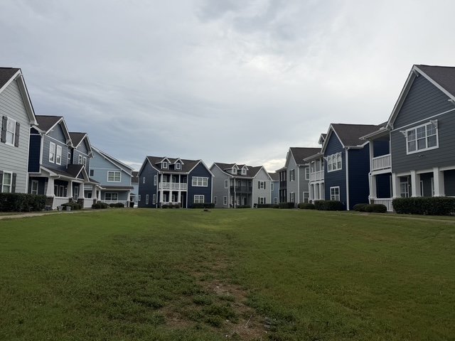 A grassy area surrounded by blue and gray apartment buildings with white trim under a cloudy sky.