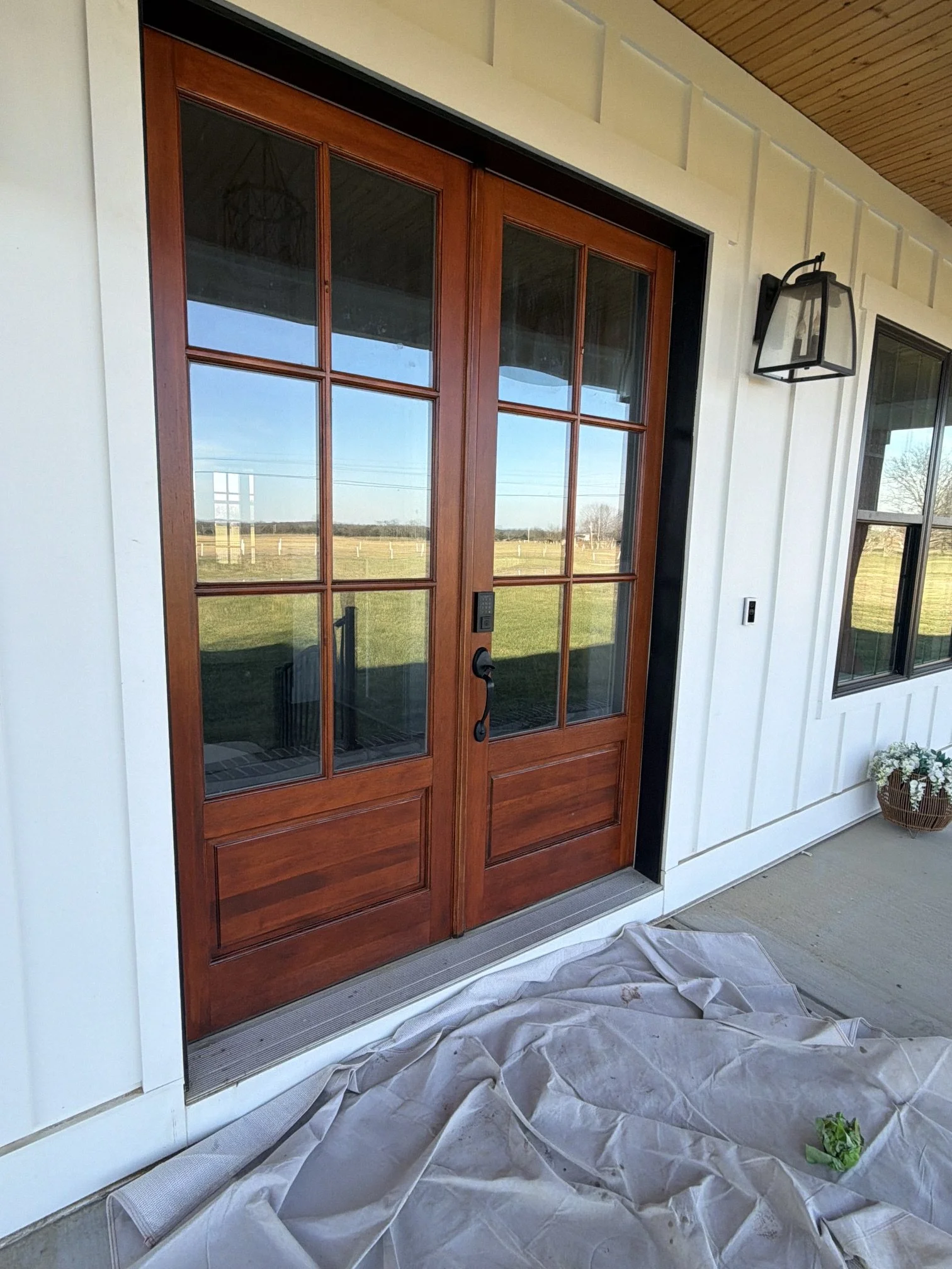 Close-up of a front door made of wood and glass panels, leading to the exterior of a house, with a screen door in front, and an outdoor wall lantern light fixture to the right.