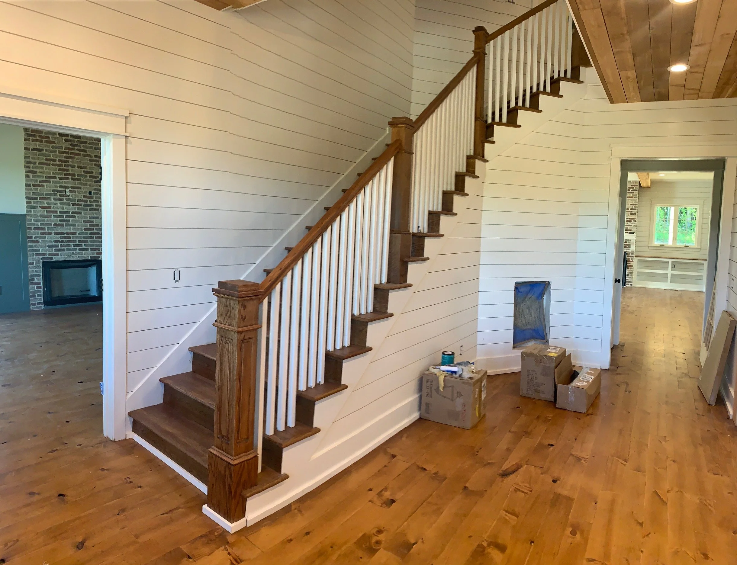 Interior view of a house under construction with a wooden staircase, hardwood floors, and unfinished boxes on the floor.